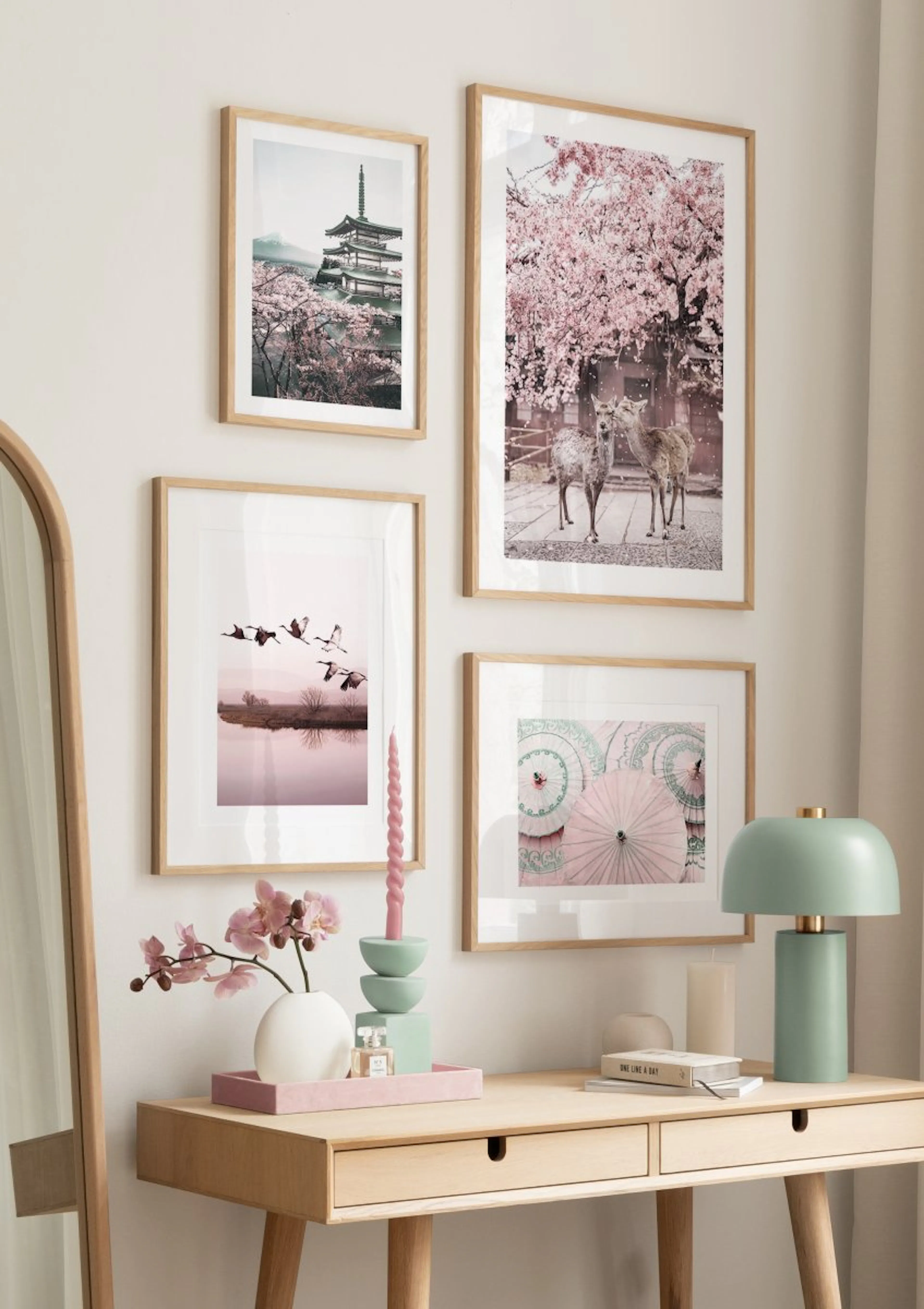 A gallery wall with four posters in a room above a wooden desk. Prints include a temple, deer, flying birds, and pink umbrellas.