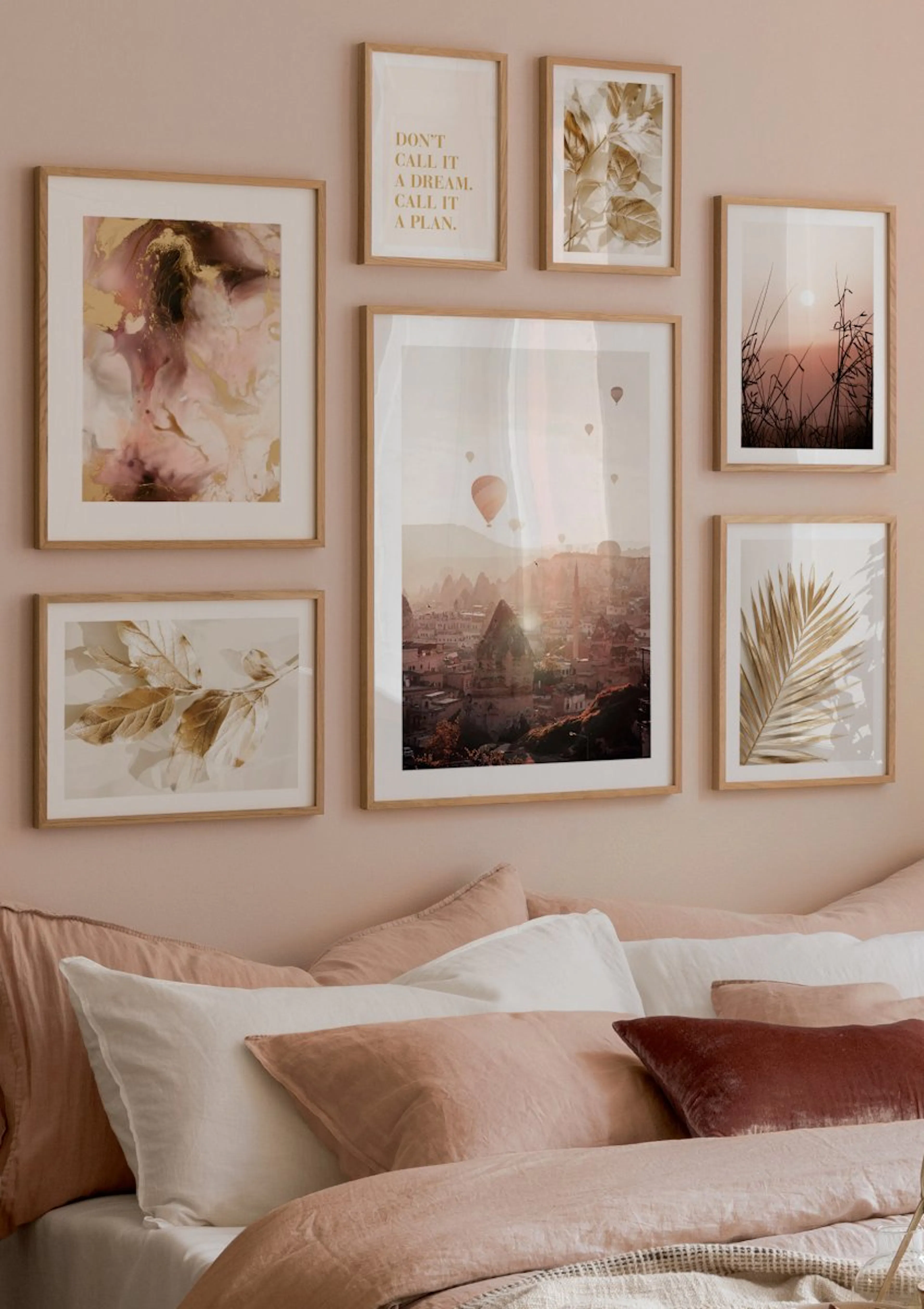 Eine Bilderwand mit Postern in Gold, Rosa und Naturtönen über einem Bett mit rosa und weißen Kissen.