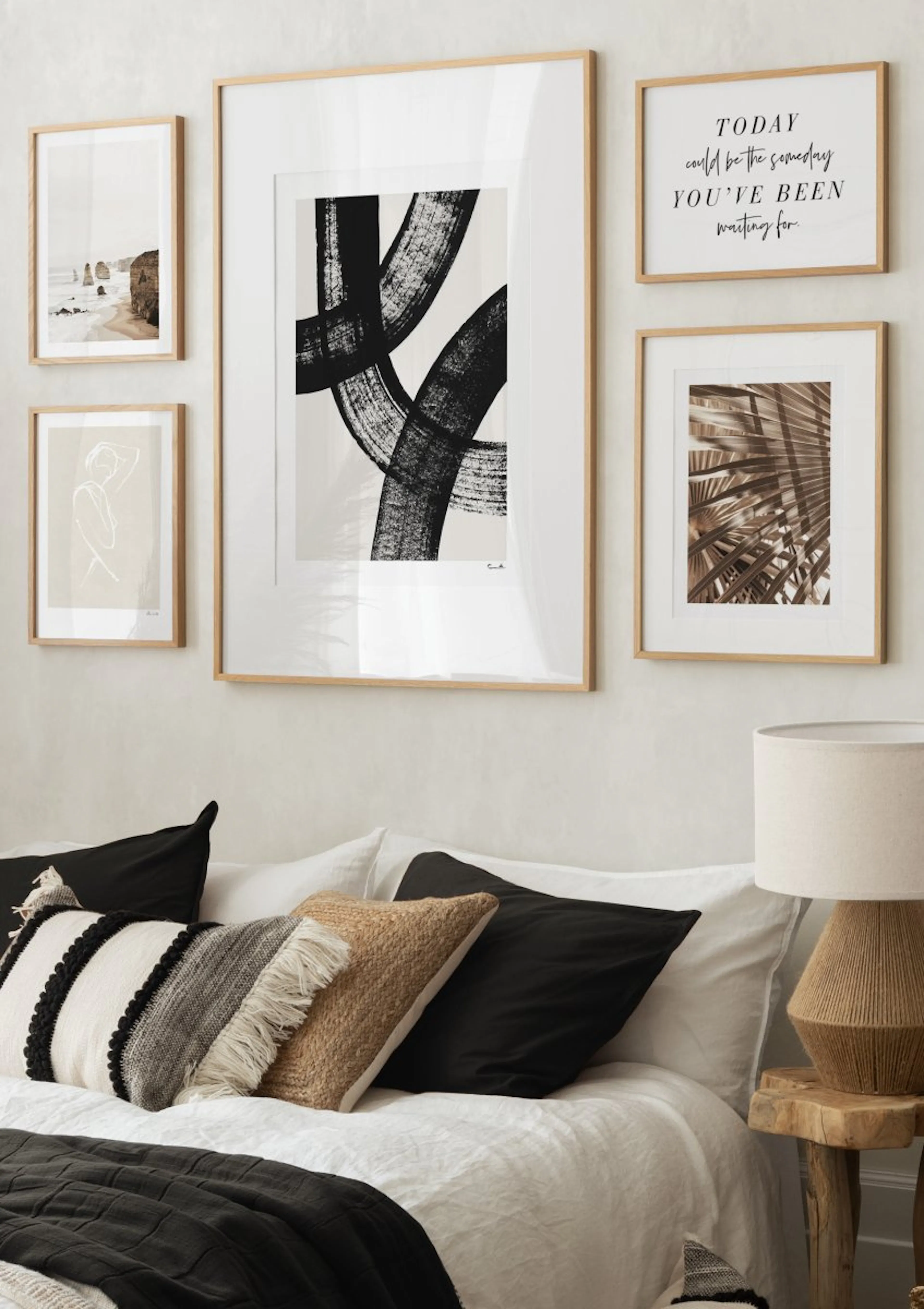 An abstract poster with bold black brushstrokes on a light background, displayed on a gallery wall above a bed.
