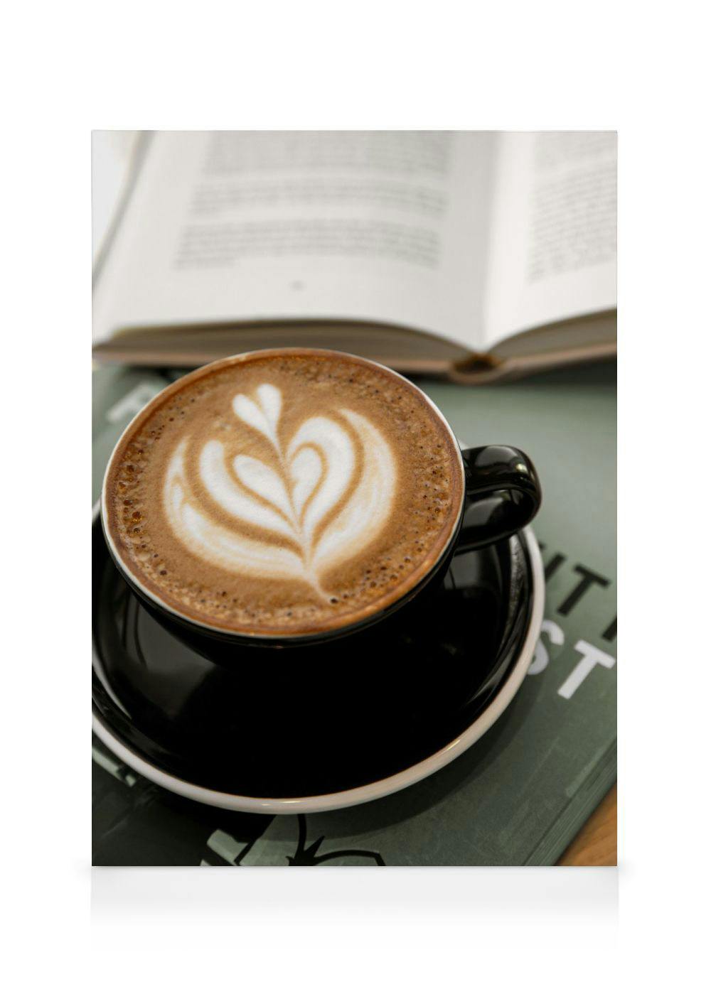 Leinwandbild mit einer Tasse Cappuccino mit Herzmotiv, die auf einem dunklen Buch steht, im Hintergrund ein offenes Buch.