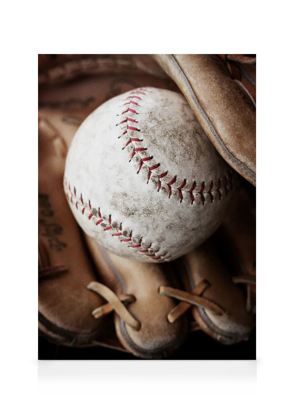 A close-up canvas of a well-worn baseball with red stitching resting in a brown leather baseball glove.