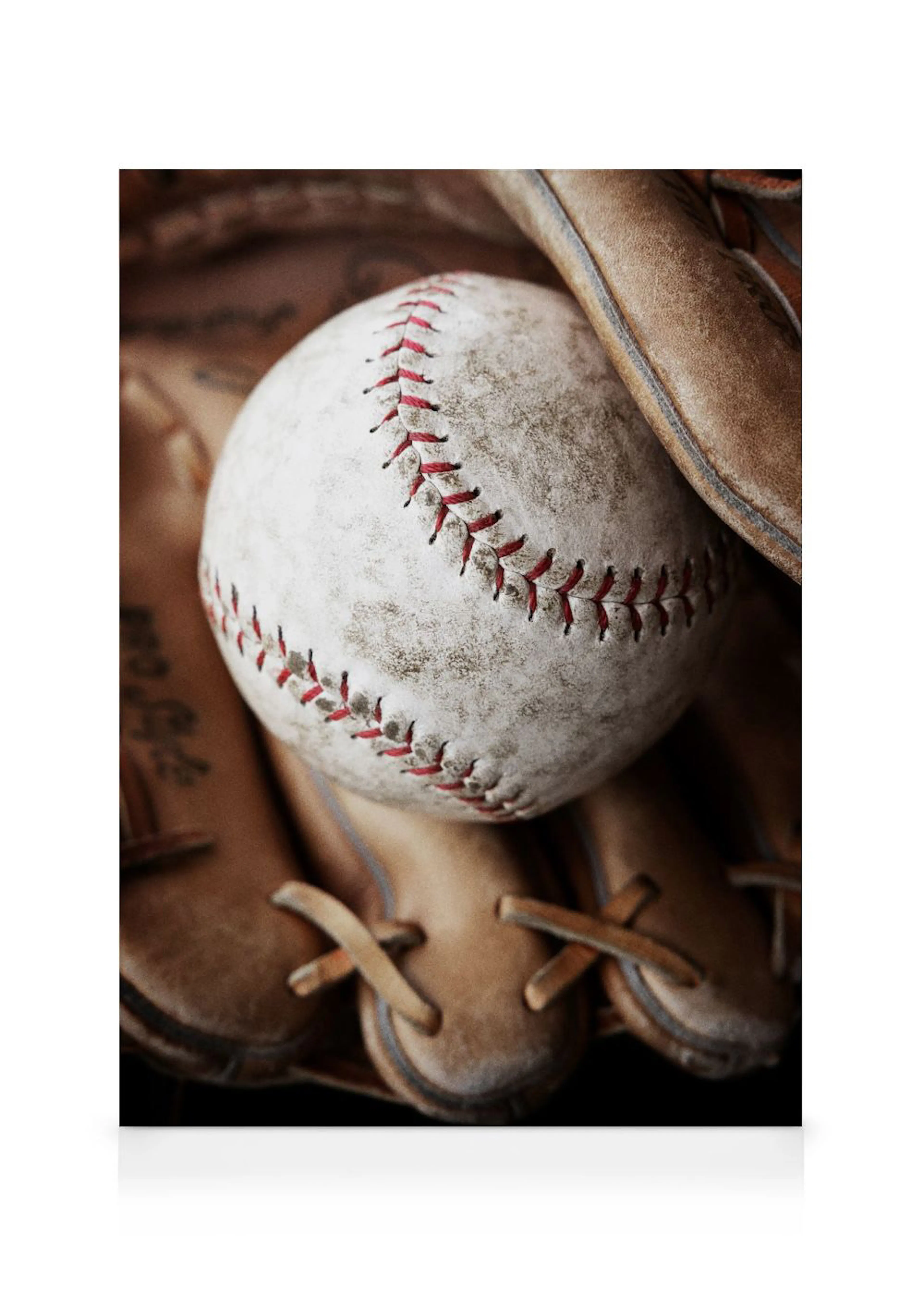 A close-up canvas of a well-worn baseball with red stitching resting in a brown leather baseball glove.