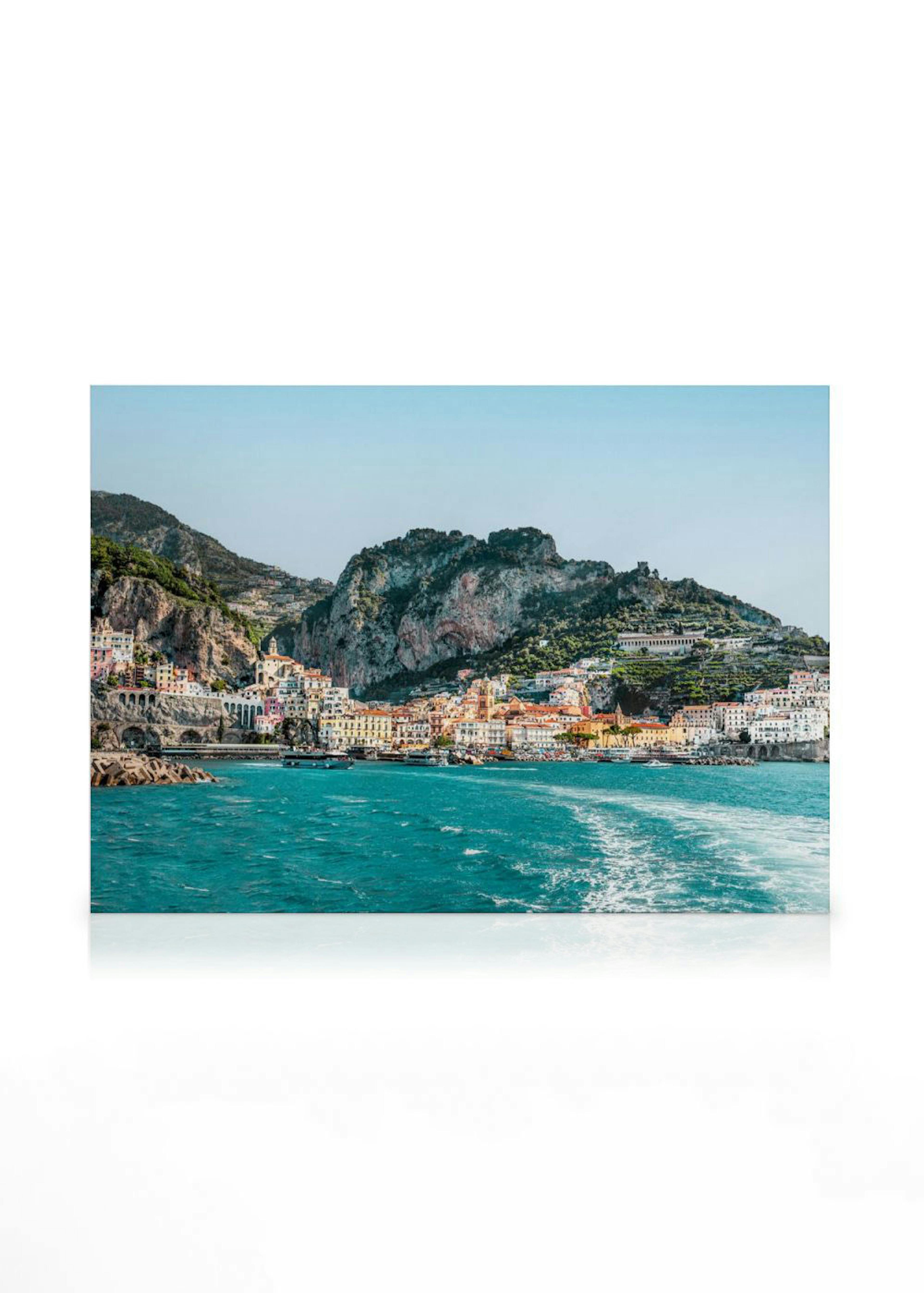 Canvas van een kustplaats met kleurrijke huizen tegen bergen, grenzend aan een turquoise zee, hangend in een lichte kamer.