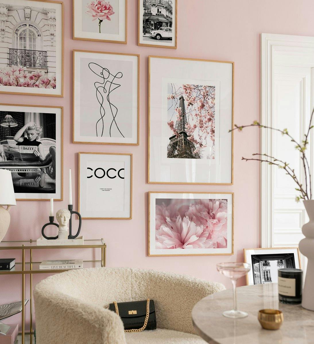 A gallery wall of posters on a pink wall, including a Paris balcony with pink flowers, an Eiffel Tower with cherry blossoms, a b