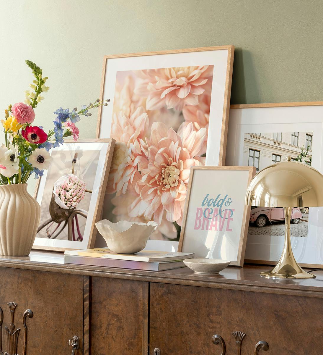 A gallery wall featuring a large peach dahlia, a bicycle with tulips, a pink car, and bold & brave text.