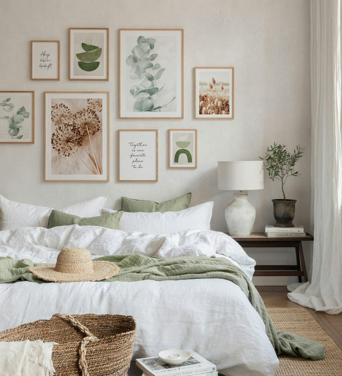 Verschillende posters met eucalyptus, bloemen en abstracte vormen in aardetinten en groen, boven een bed.