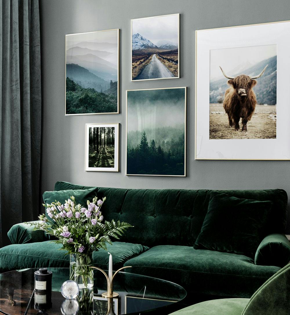 A gallery wall with five nature-themed posters, including mountains, forests, a road, and a Highland cow, above a green sofa.