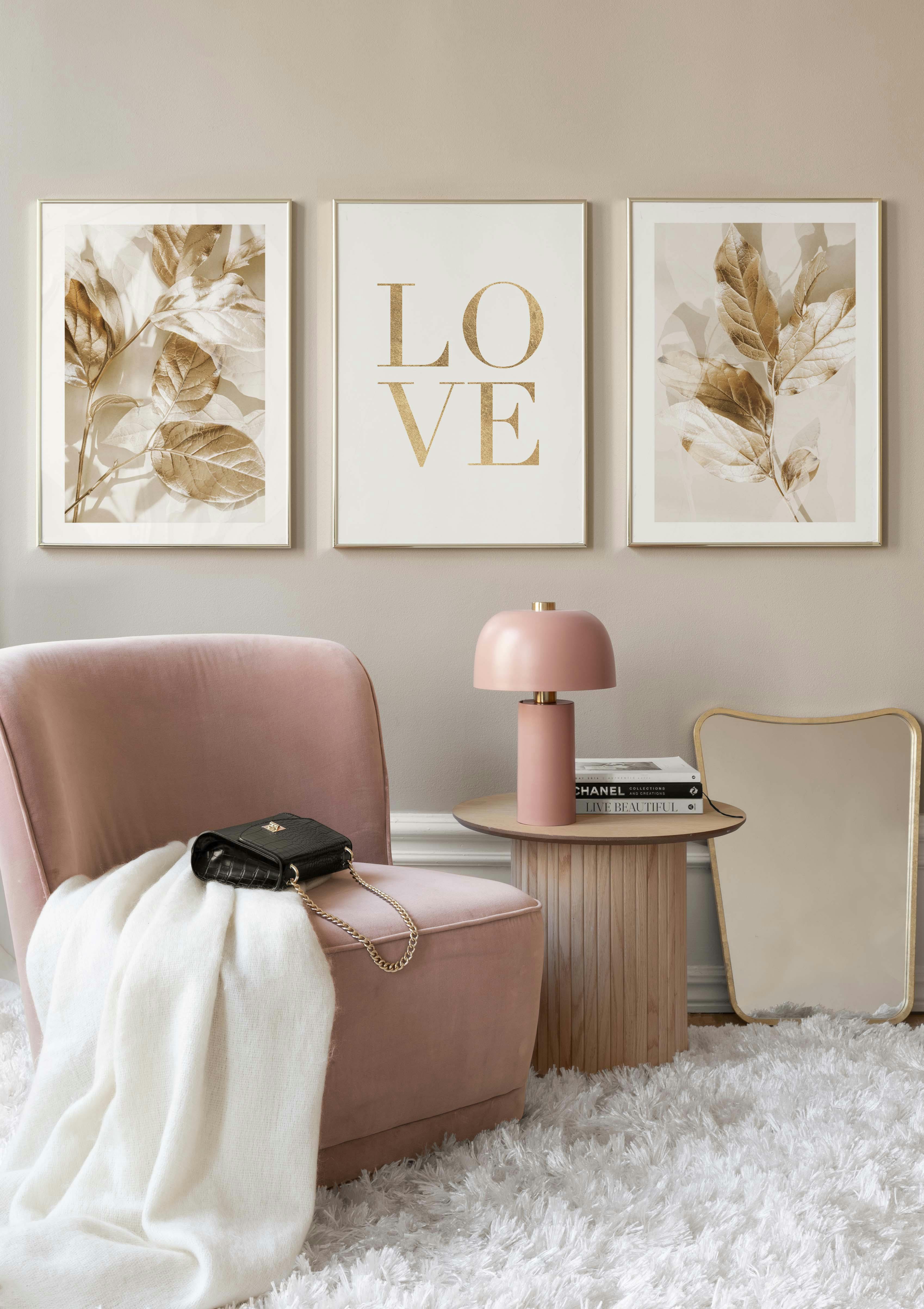 Drie postersets, twee van gouden bladeren en één met de tekst LOVE, hangen boven een roze stoel in een stijlvolle kamer.