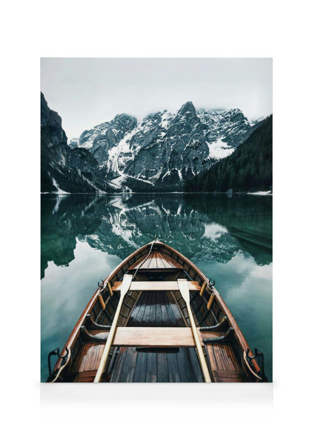 Toile dun bateau en bois sur un lac reflétant des montagnes enneigées et des forêts sombres.