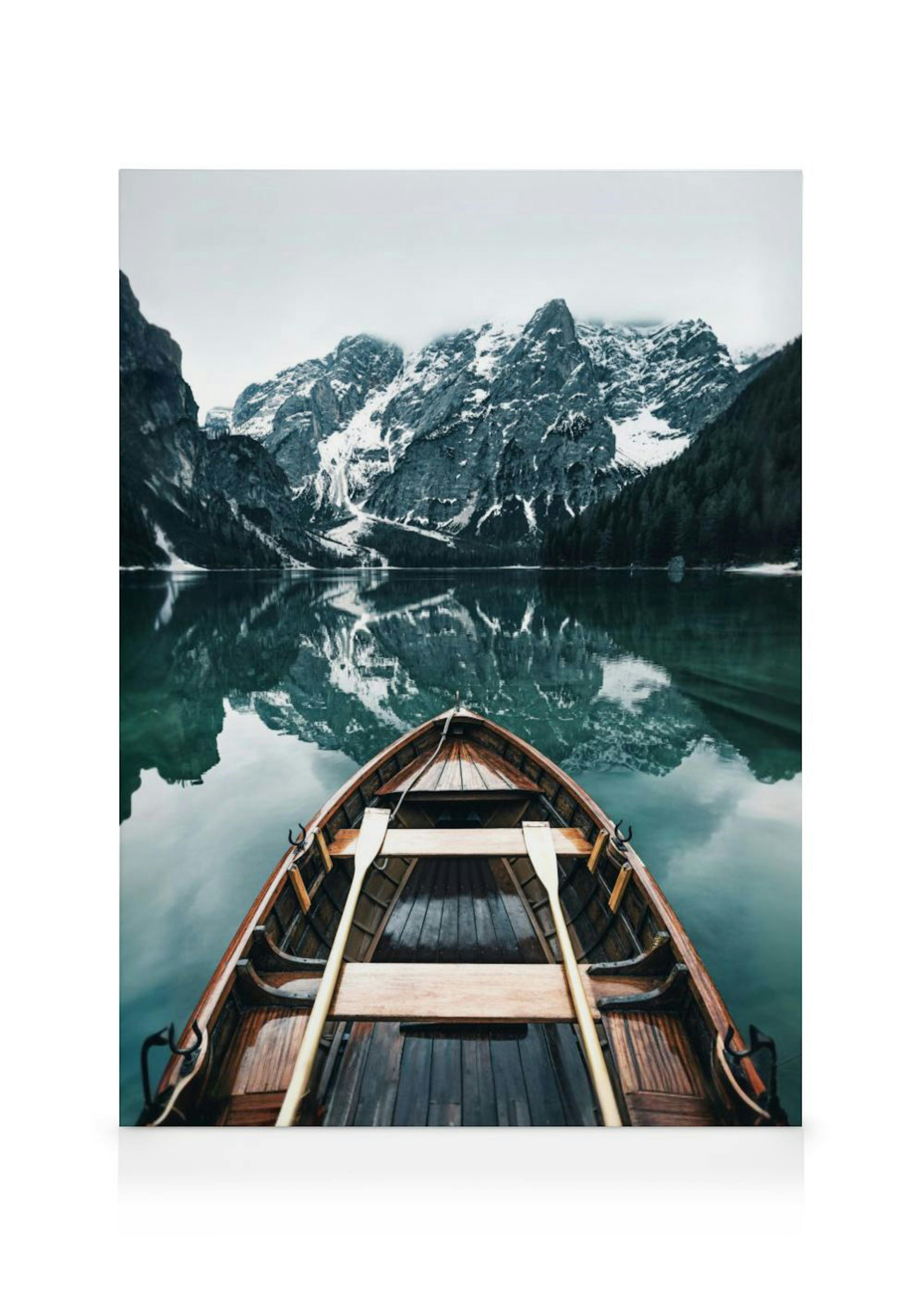 Toile dun bateau en bois sur un lac reflétant des montagnes enneigées et des forêts sombres.