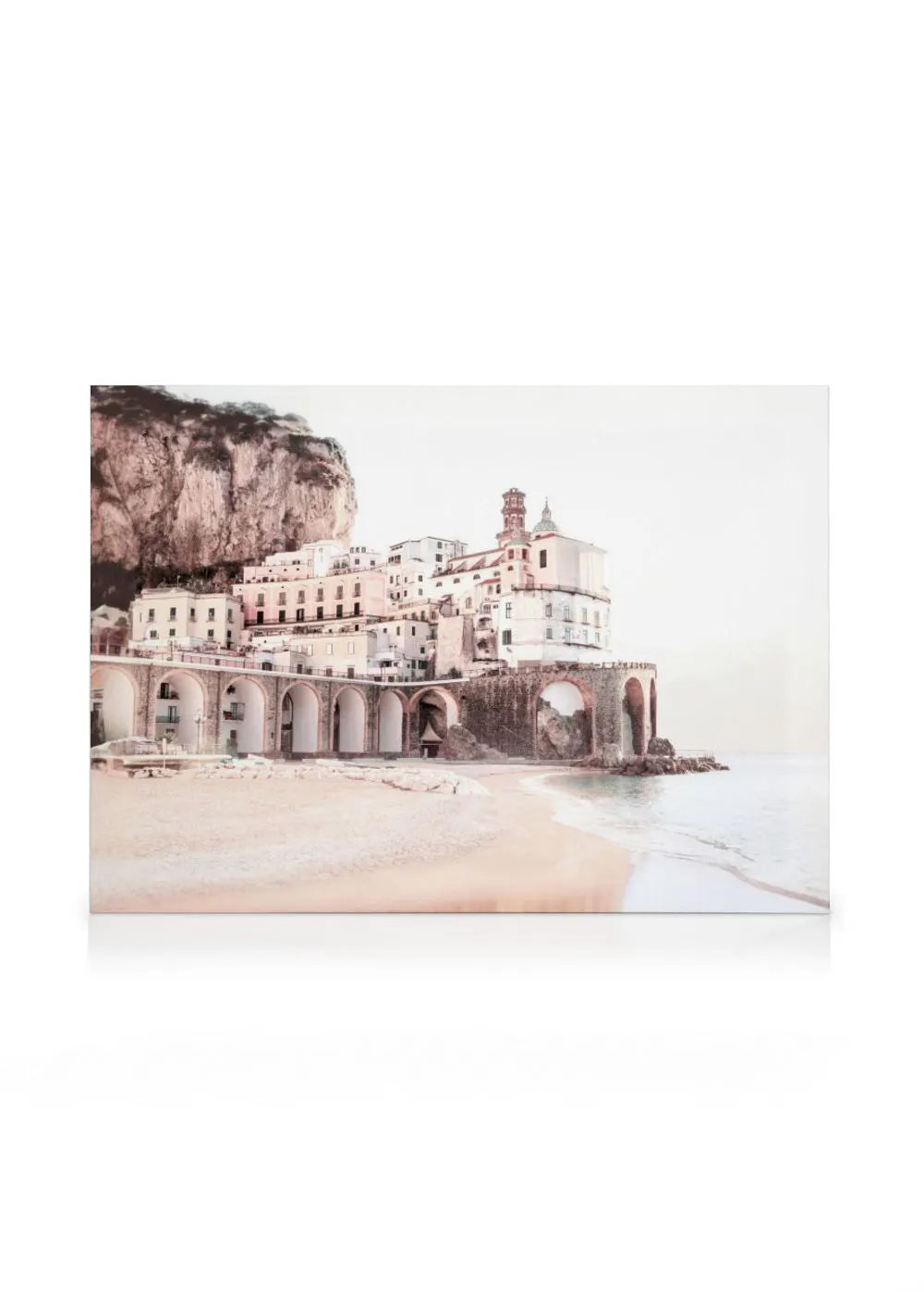 A canvas showing a town with white and peach buildings and archways, nestled against a cliff by a sandy beach and calm sea.