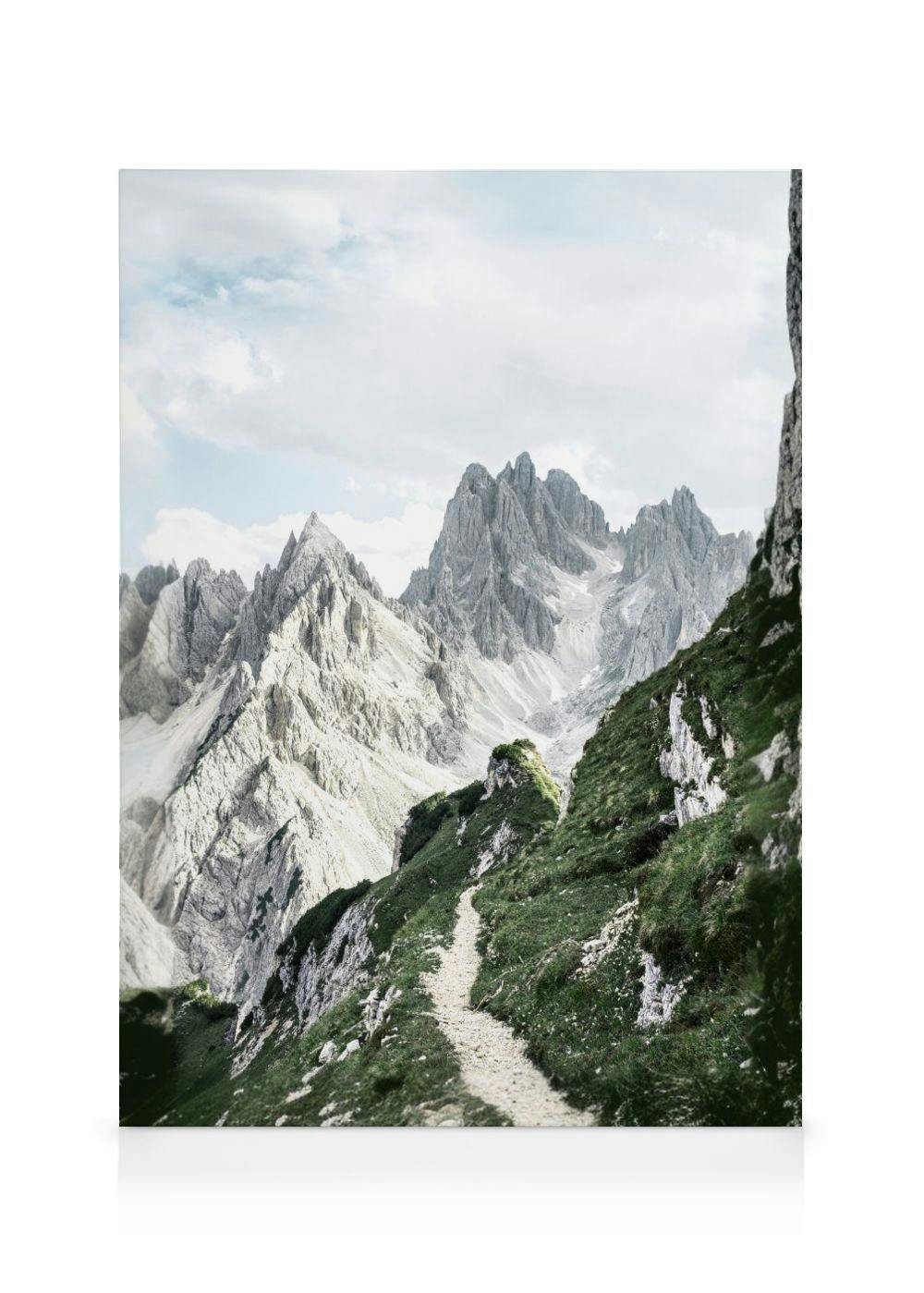 Leinwandbild eines Bergpfades in den Dolomiten mit schroffen Felsformationen und grünen Hängen unter bewölktem Himmel.