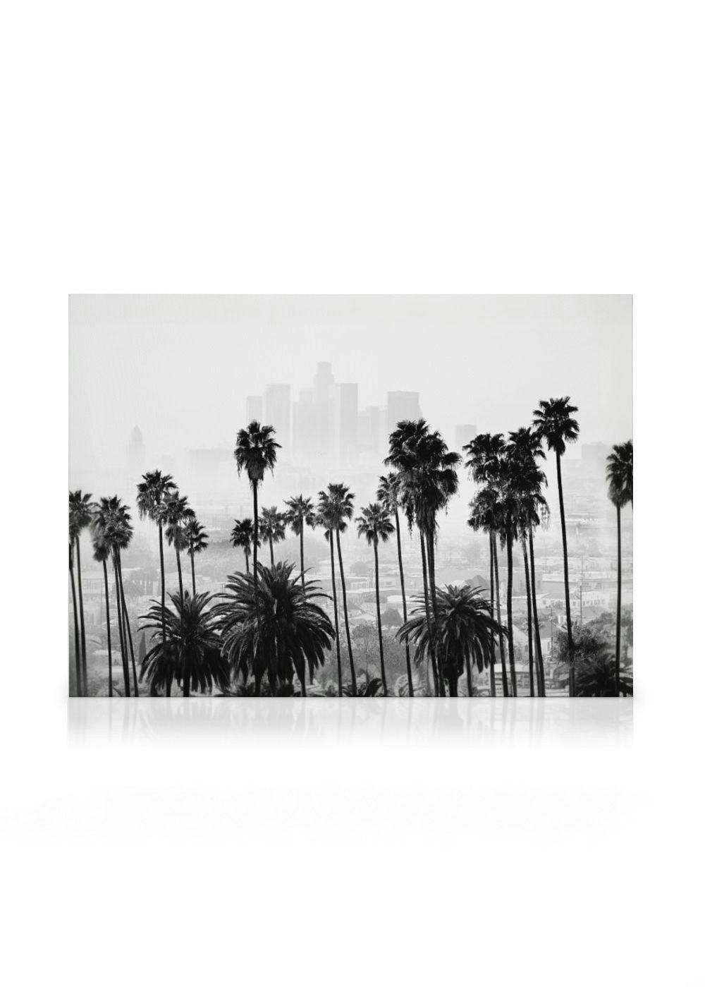 Toile noir et blanc dune rangée de palmiers devant lhorizon brumeux dune ville.