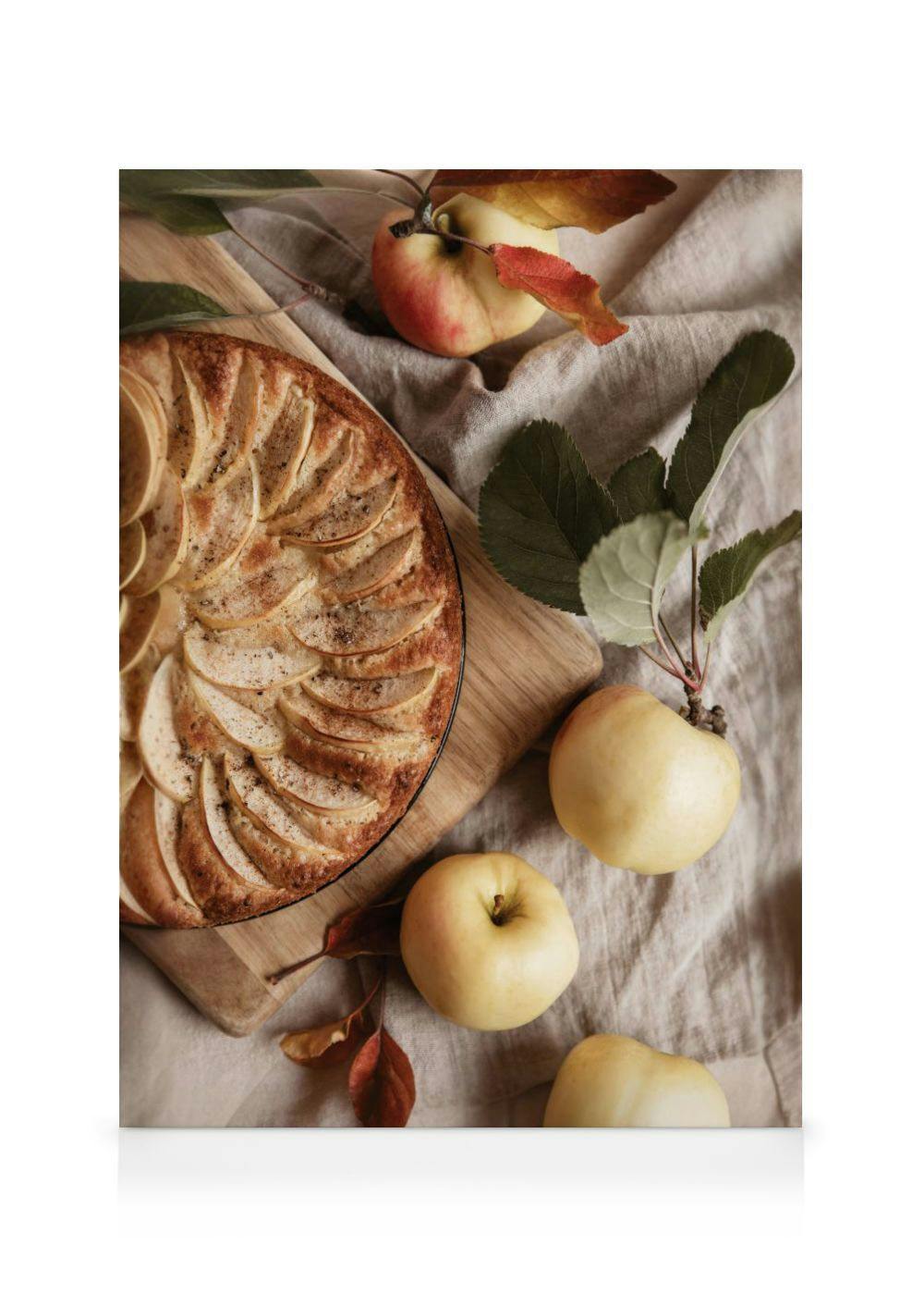 A canvas print featuring an apple pie with sliced apples on top, next to fresh red and yellow apples on a linen cloth.