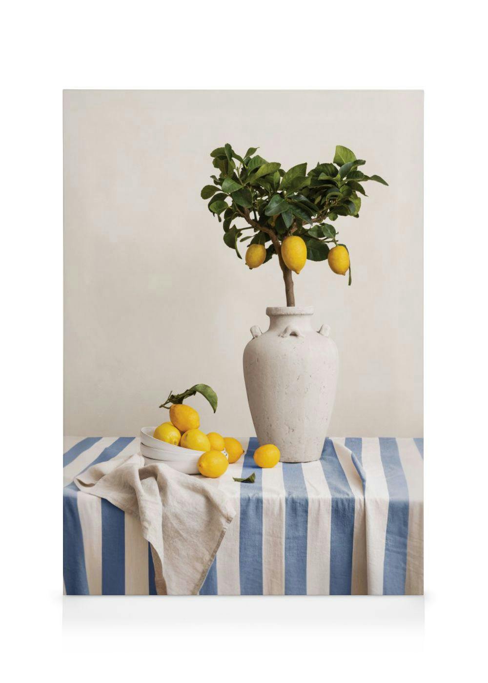 A still life canvas of a small lemon tree in a large white vase, with a bowl of lemons on a blue and white striped tablecloth.