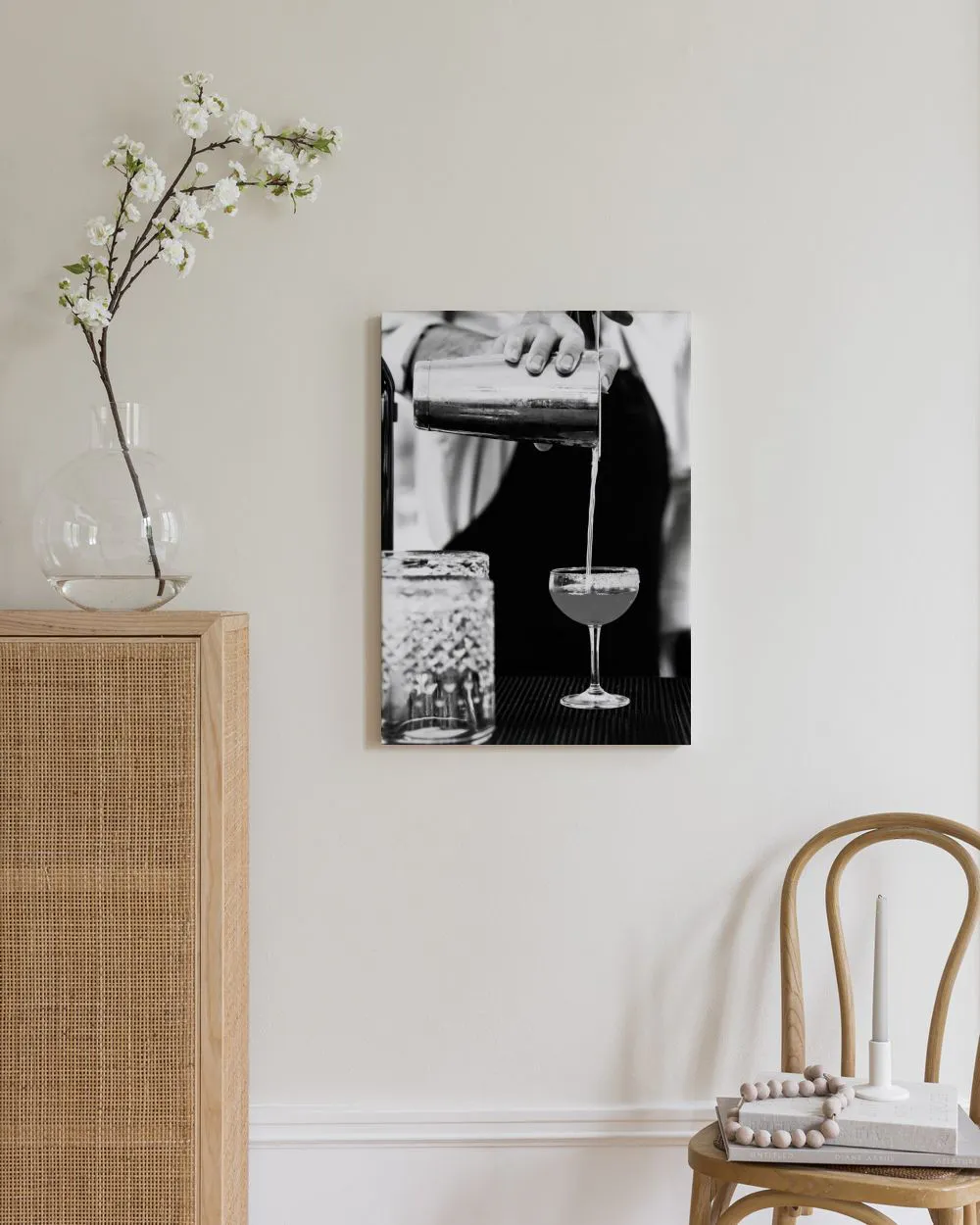 Toile noir et blanc d’un barman versant un cocktail, accrochée dans un salon moderne avec un meuble en rotin clair.