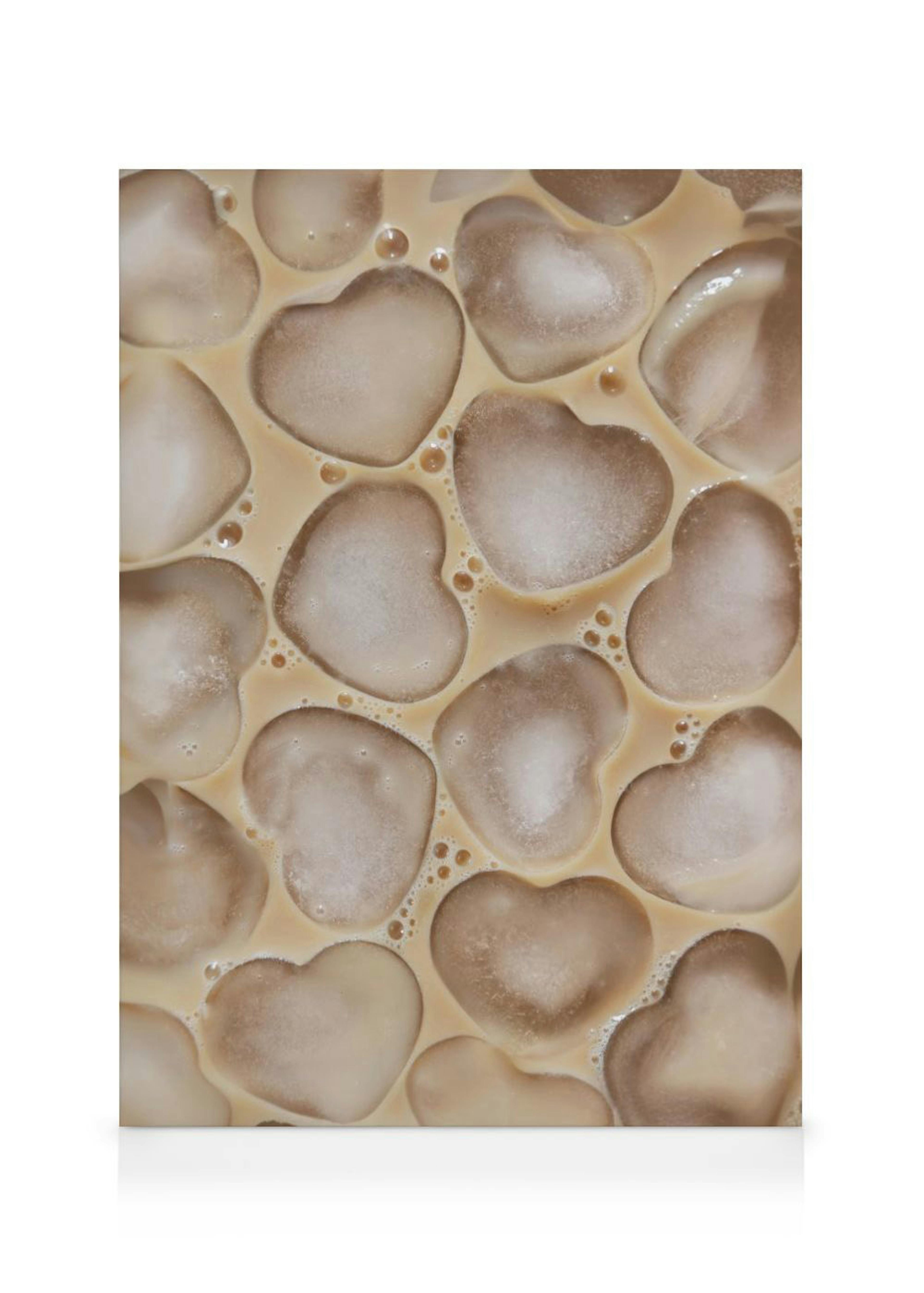 Toile avec des glaçons en forme de cœur flottant dans un liquide beige clair, avec des bulles.