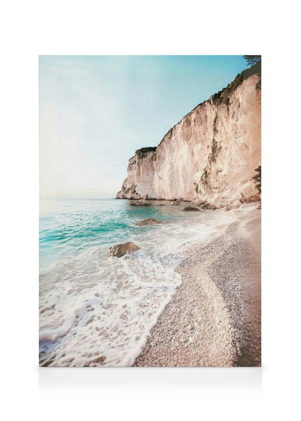 Toile de la mer turquoise longeant une plage de galets, avec une falaise rocheuse imposante sous un ciel clair.