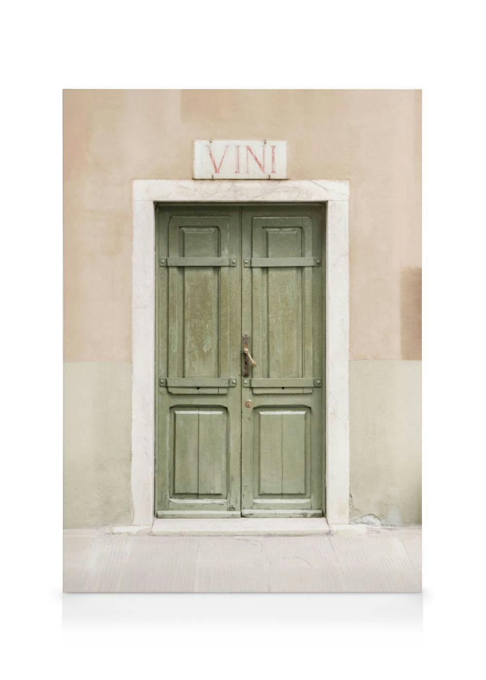 Toile dune porte en bois vert patiné, encadrée de pierre blanche, sous une enseigne VINI sur un mur beige.