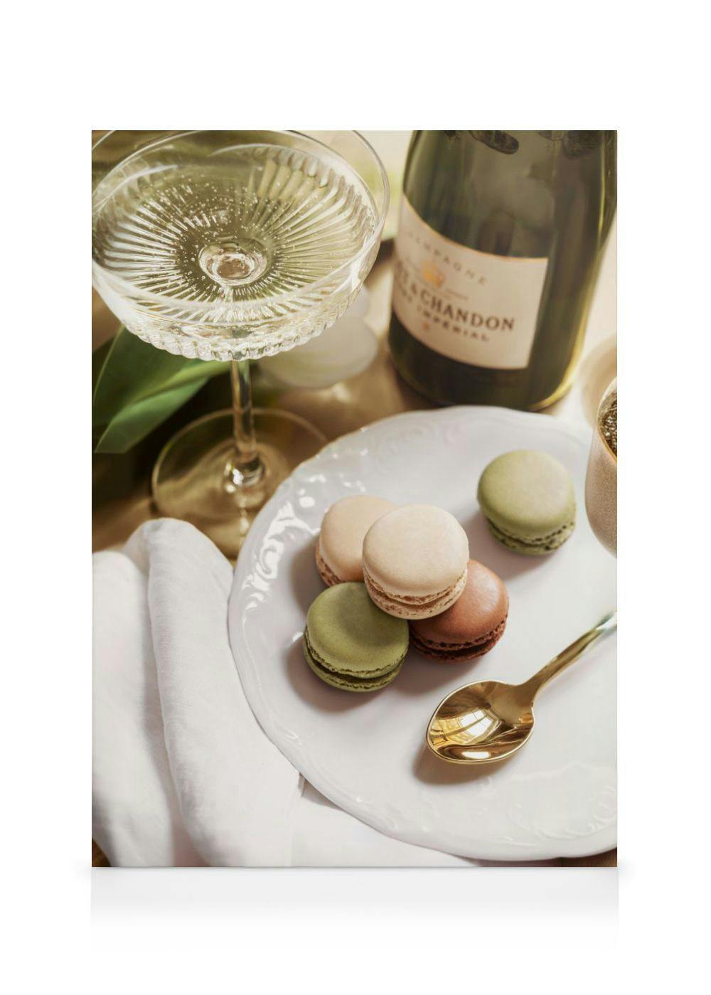 Leinwandbild mit Sektglas, Champagnerflasche und Macarons auf einem weißen Teller, daneben ein goldener Löffel.