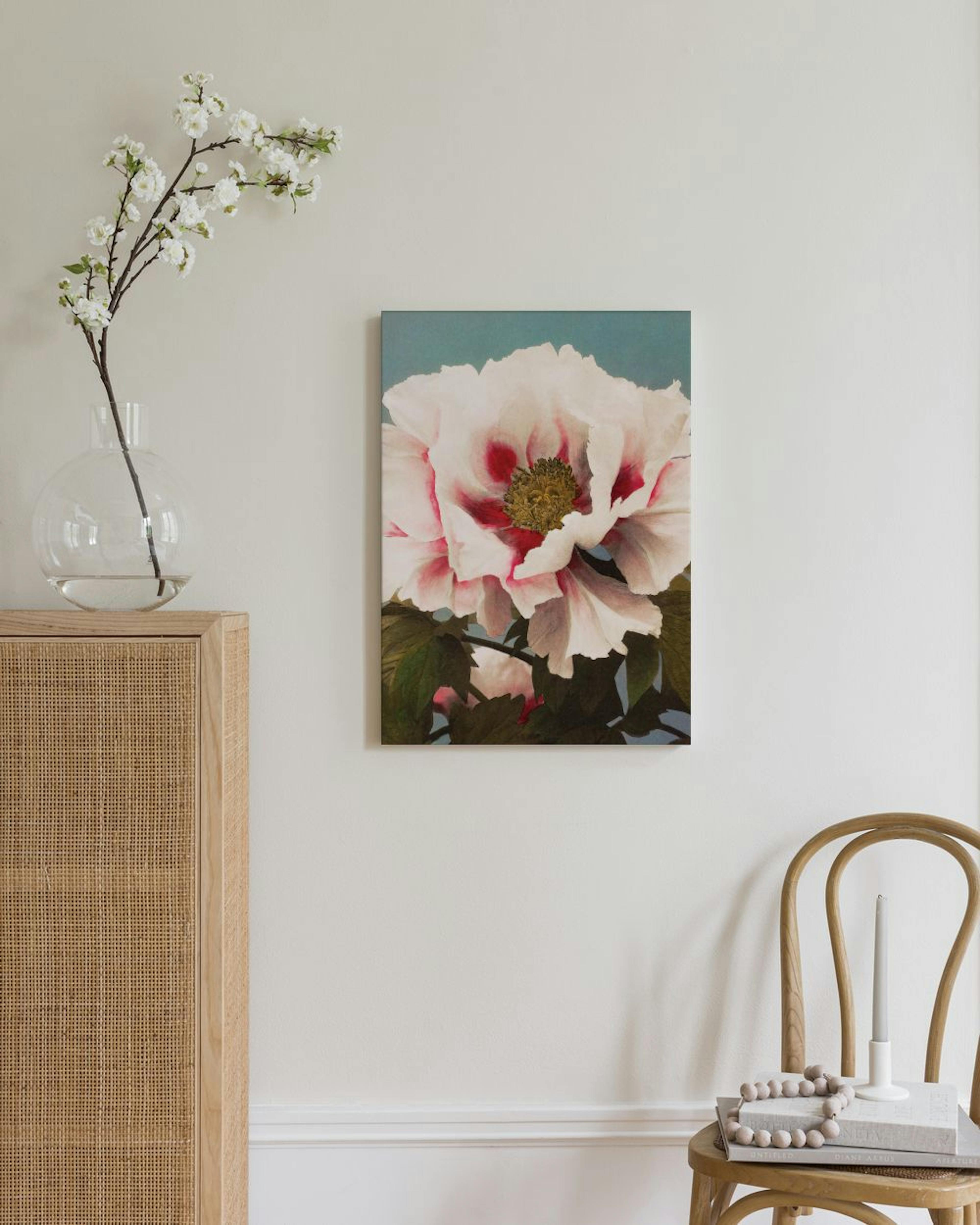 Leinwandbild einer rosa Pfingstrose mit grünen Blättern vor blauem Hintergrund, über einem Rattan-Schrank.