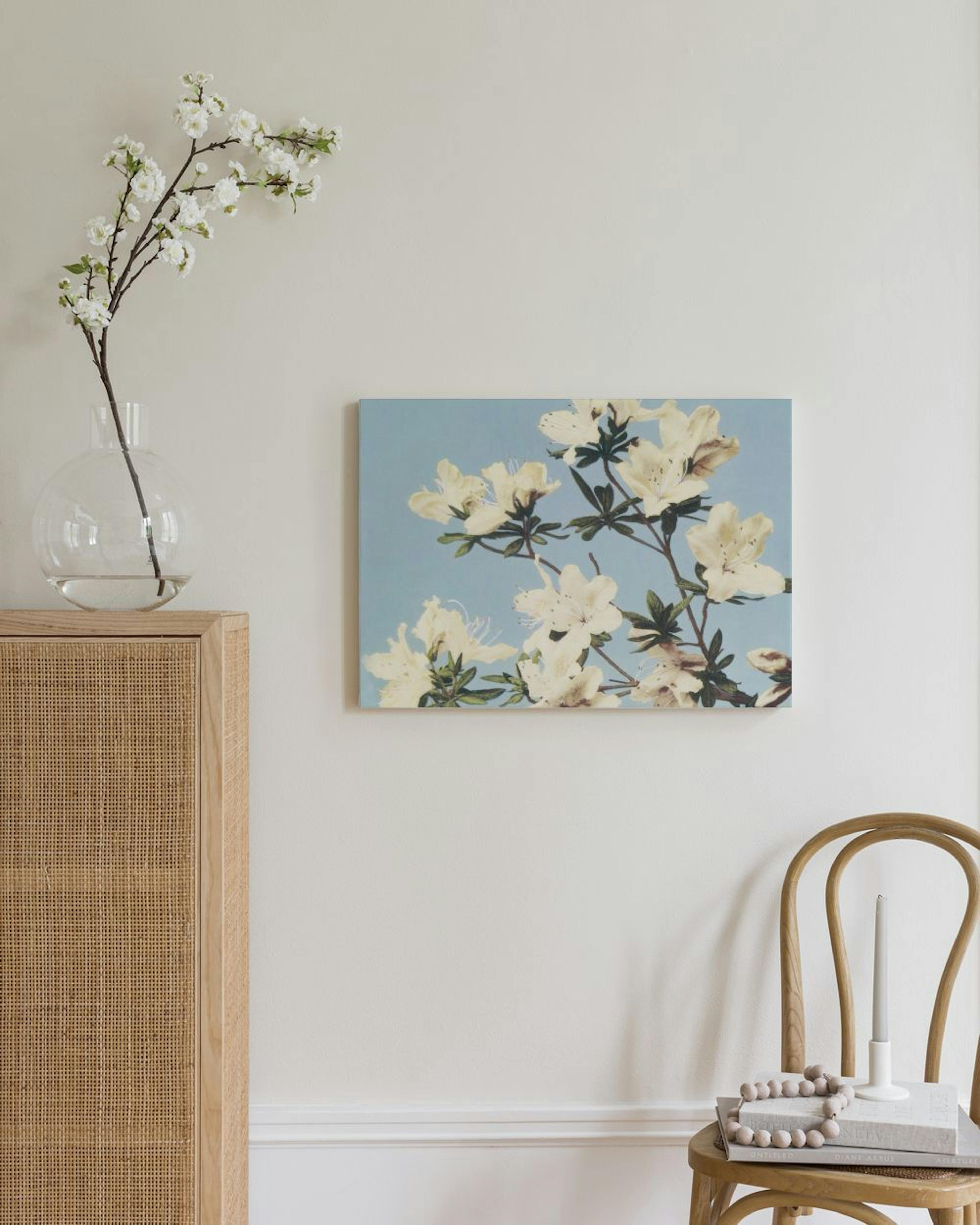 Leinwandbild mit weissen Blüten auf blauem Hintergrund, über einem Rattanschrank und Stuhl.
