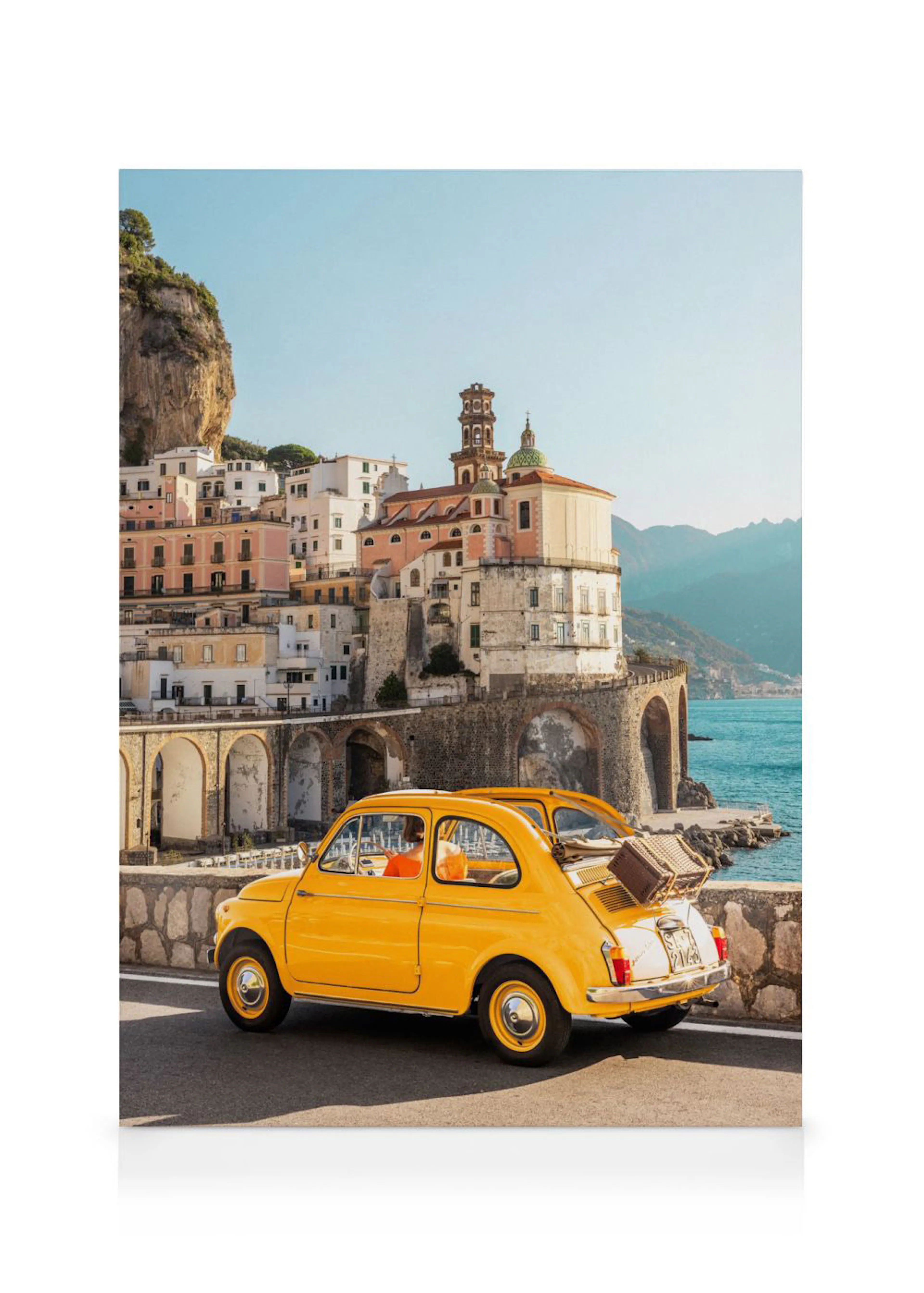 A canvas featuring a bright yellow vintage car parked on a road overlooking a cliffside village and the blue sea.
