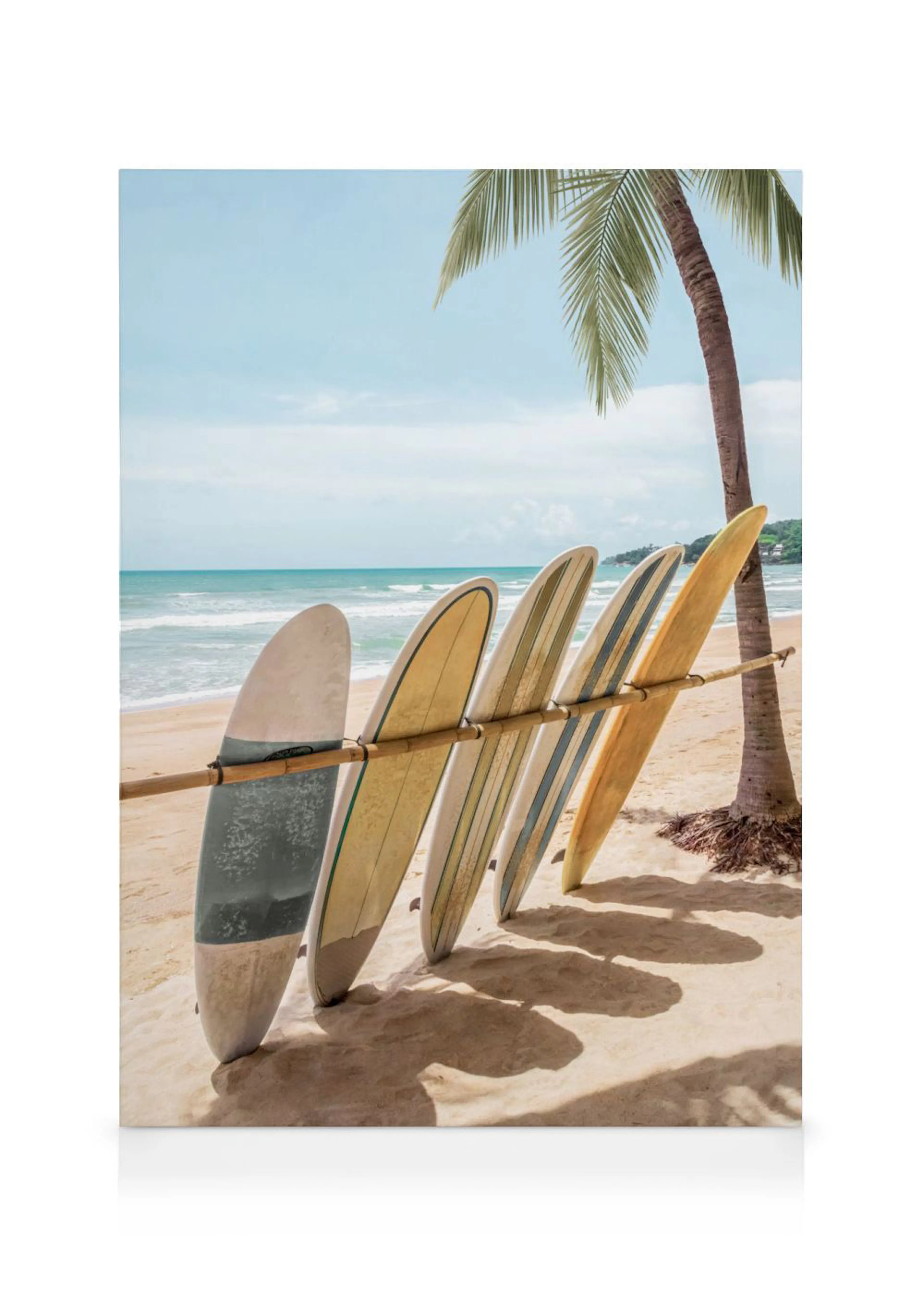 Lienzo de tablas de surf de colores pastel en una playa, apoyadas en un poste de bambú junto a una palmera.