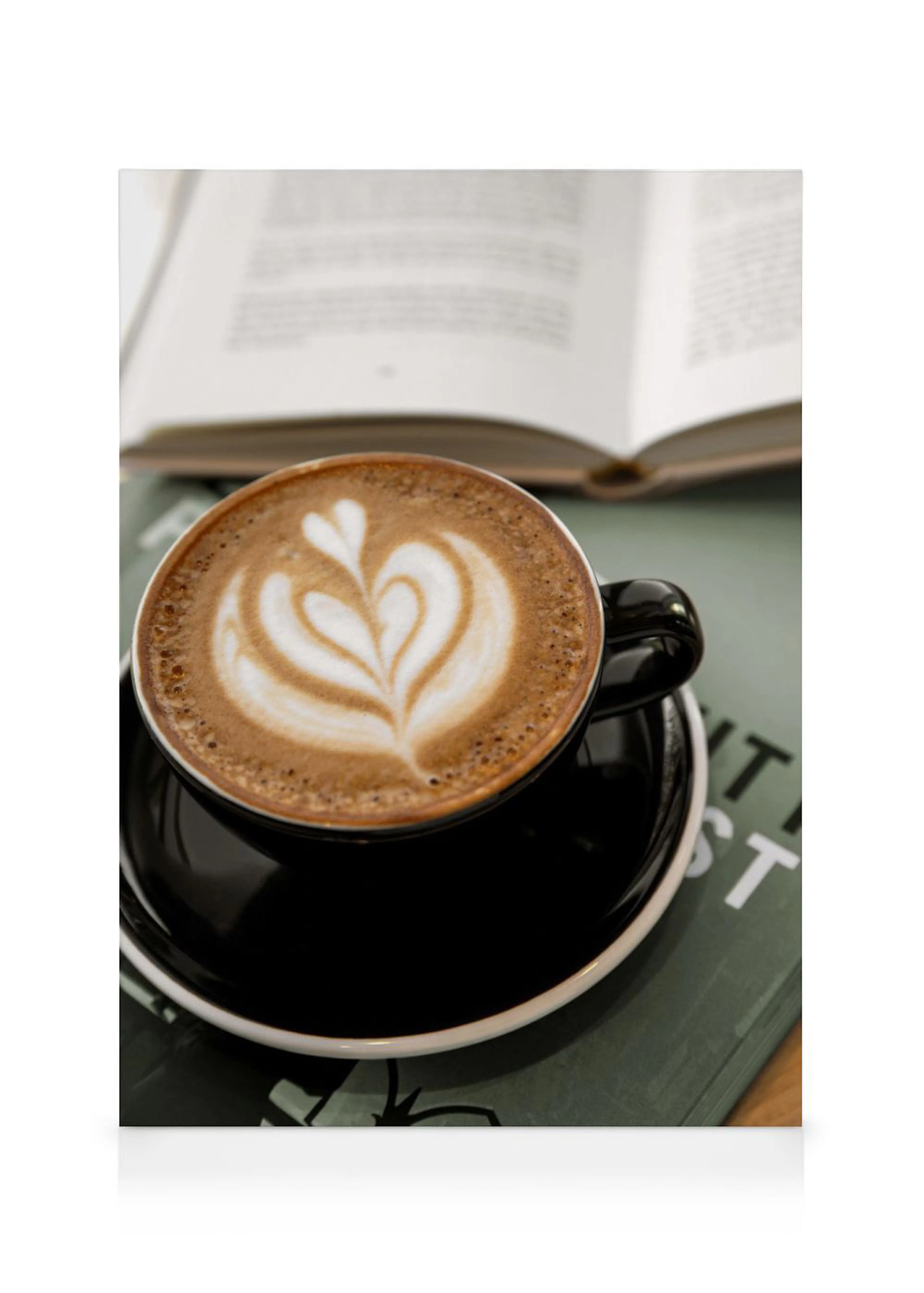 Leinwandbild mit einer Tasse Cappuccino mit Herzmotiv, die auf einem dunklen Buch steht, im Hintergrund ein offenes Buch.