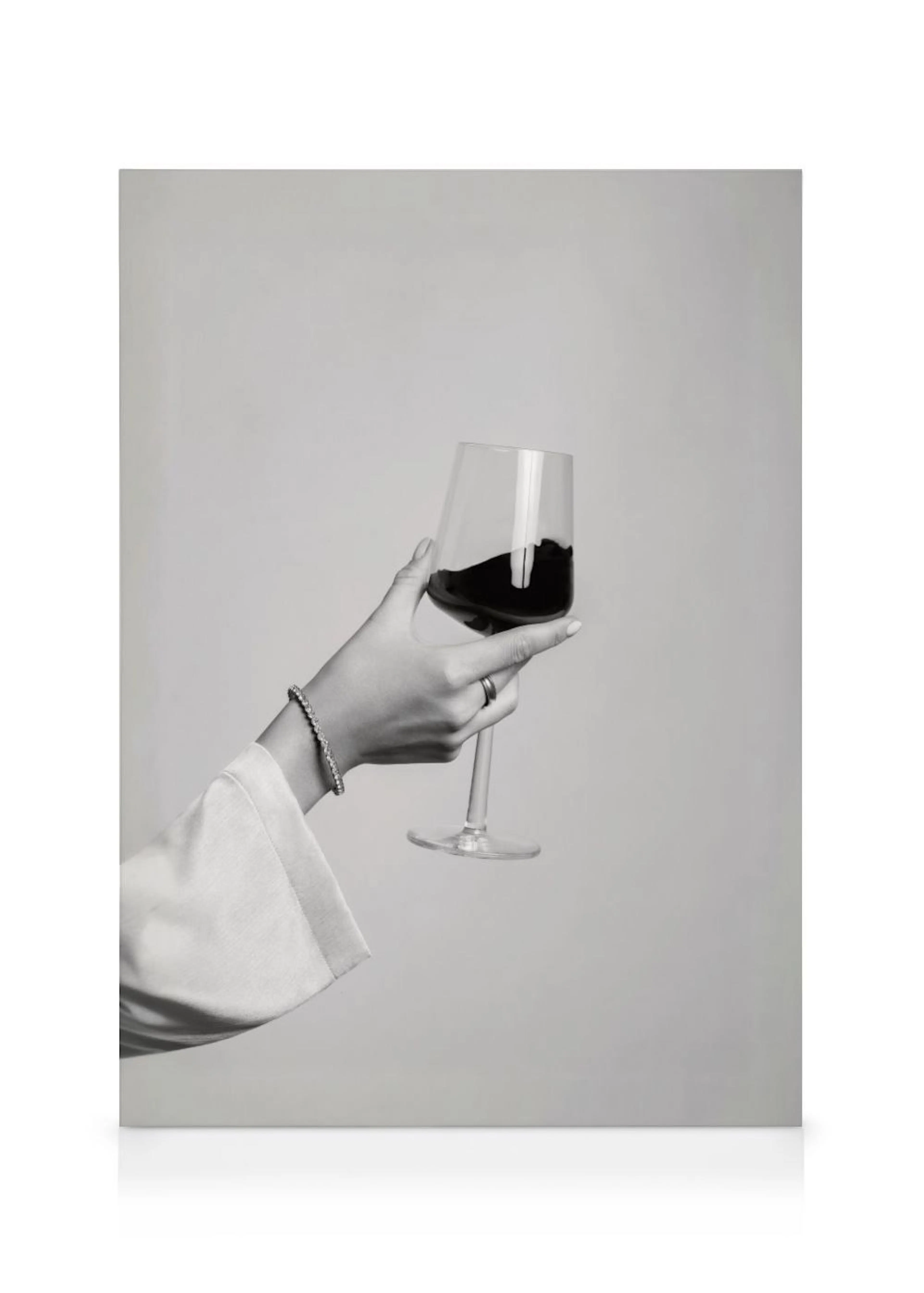 Lienzo monocromático de una mano femenina sosteniendo una copa de vino tinto sobre un fondo claro y liso.