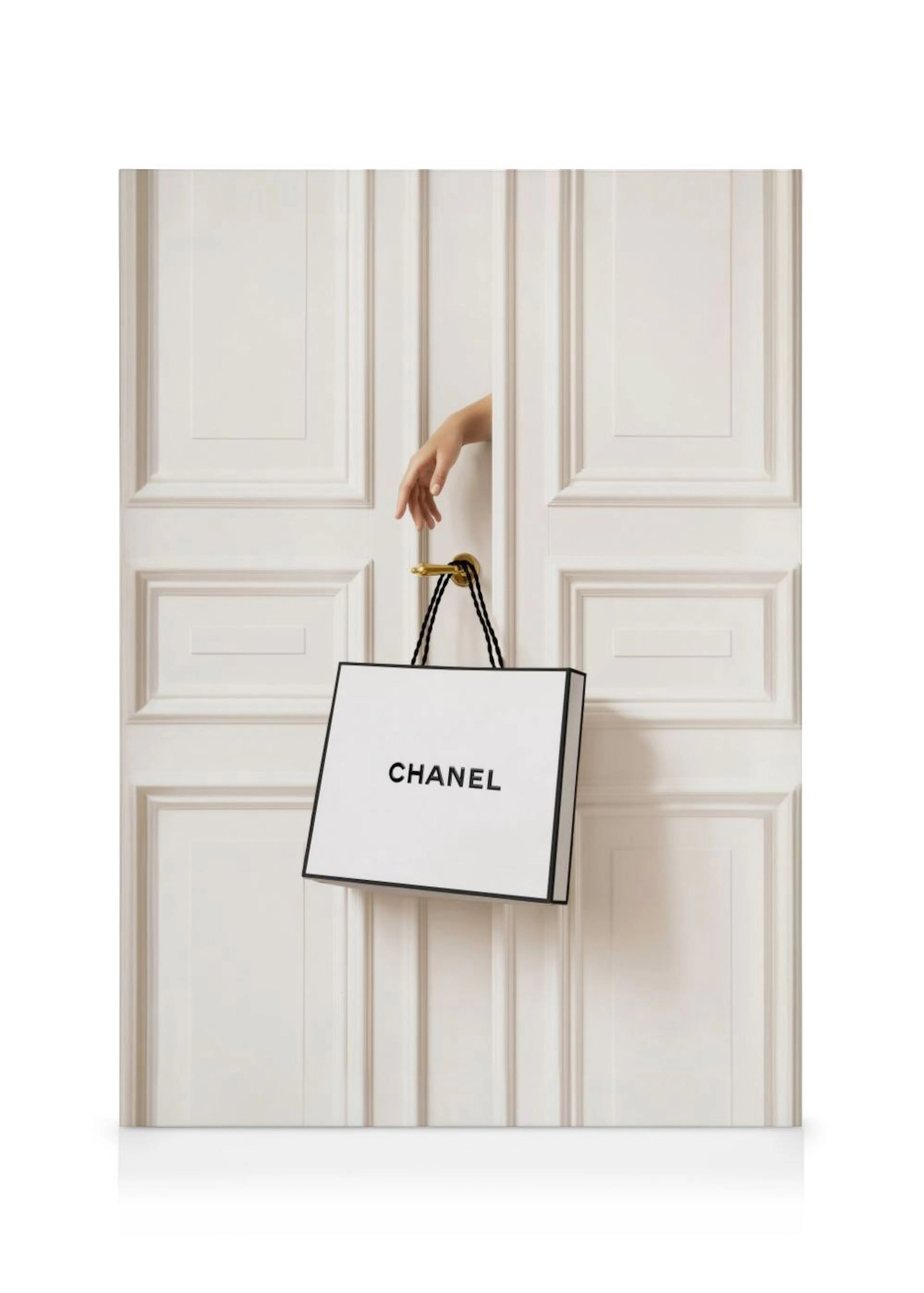 Lienzo con una mano asomándose por una puerta blanca, sosteniendo una bolsa de compra Chanel.