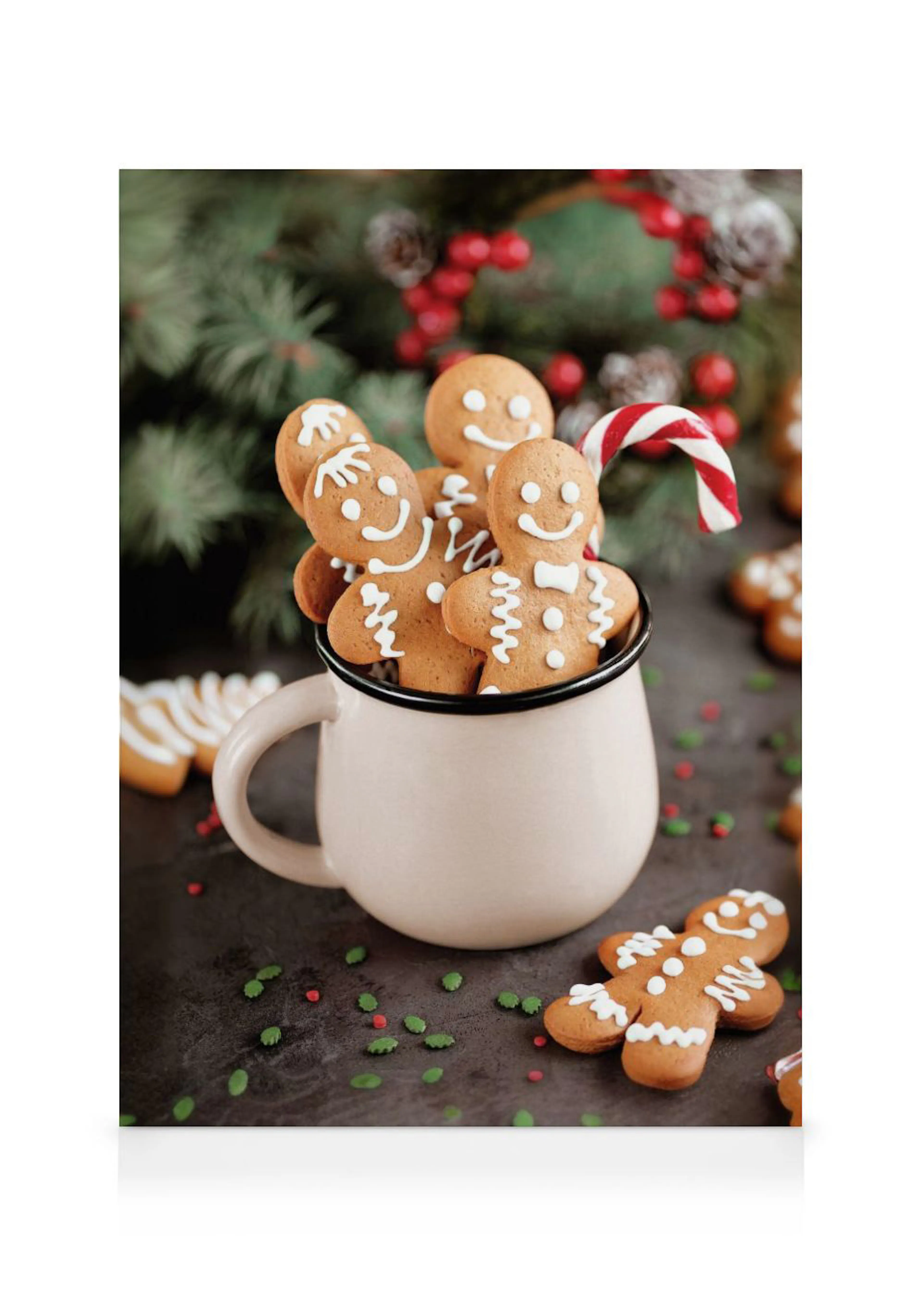 Lienzo de galletas de jengibre en una taza blanca con un bastón de caramelo, sobre una superficie oscura con decoraciones navide
