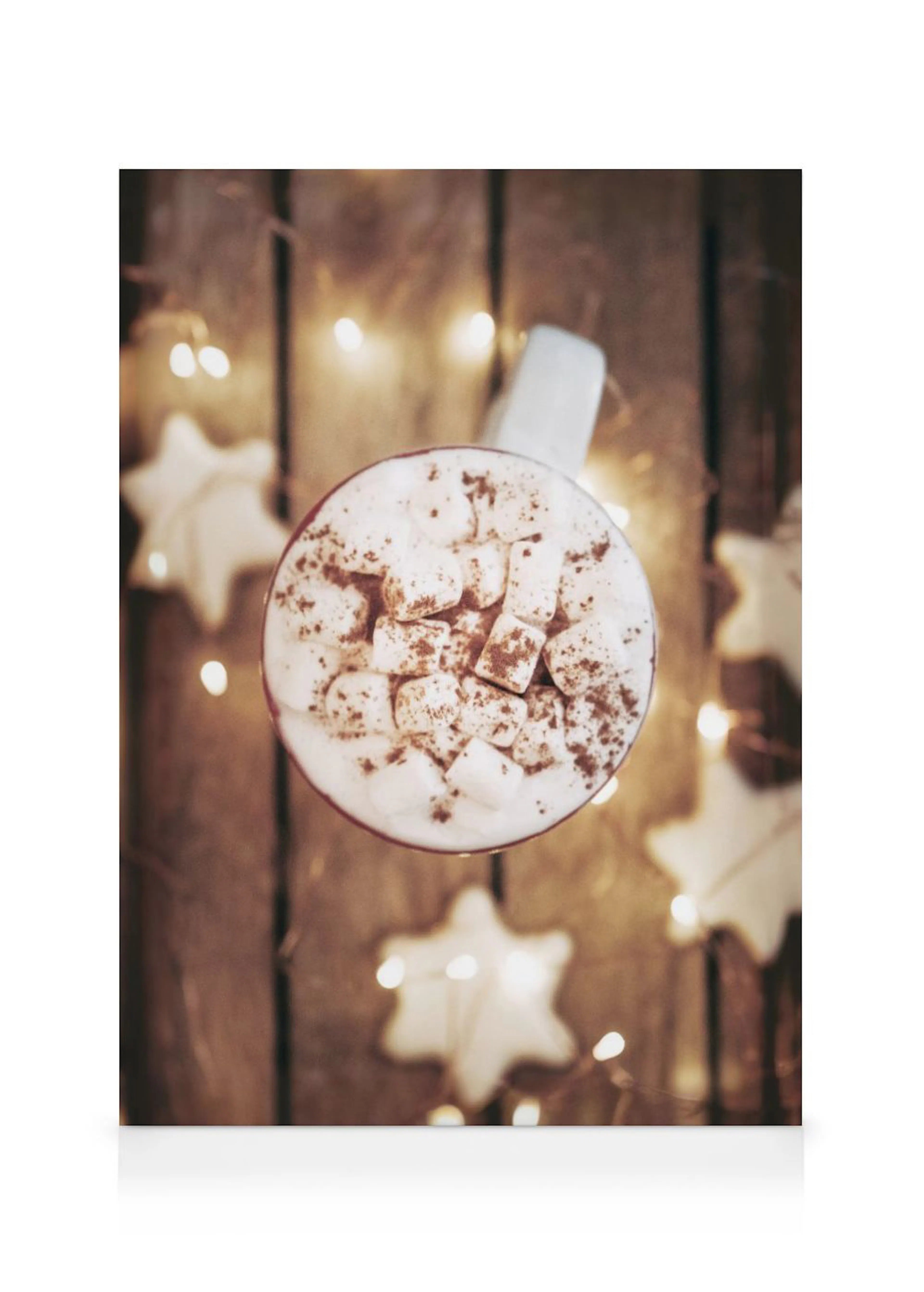 A festive canvas of hot chocolate with marshmallows and cocoa powder, surrounded by star-shaped cookies and warm string lights.