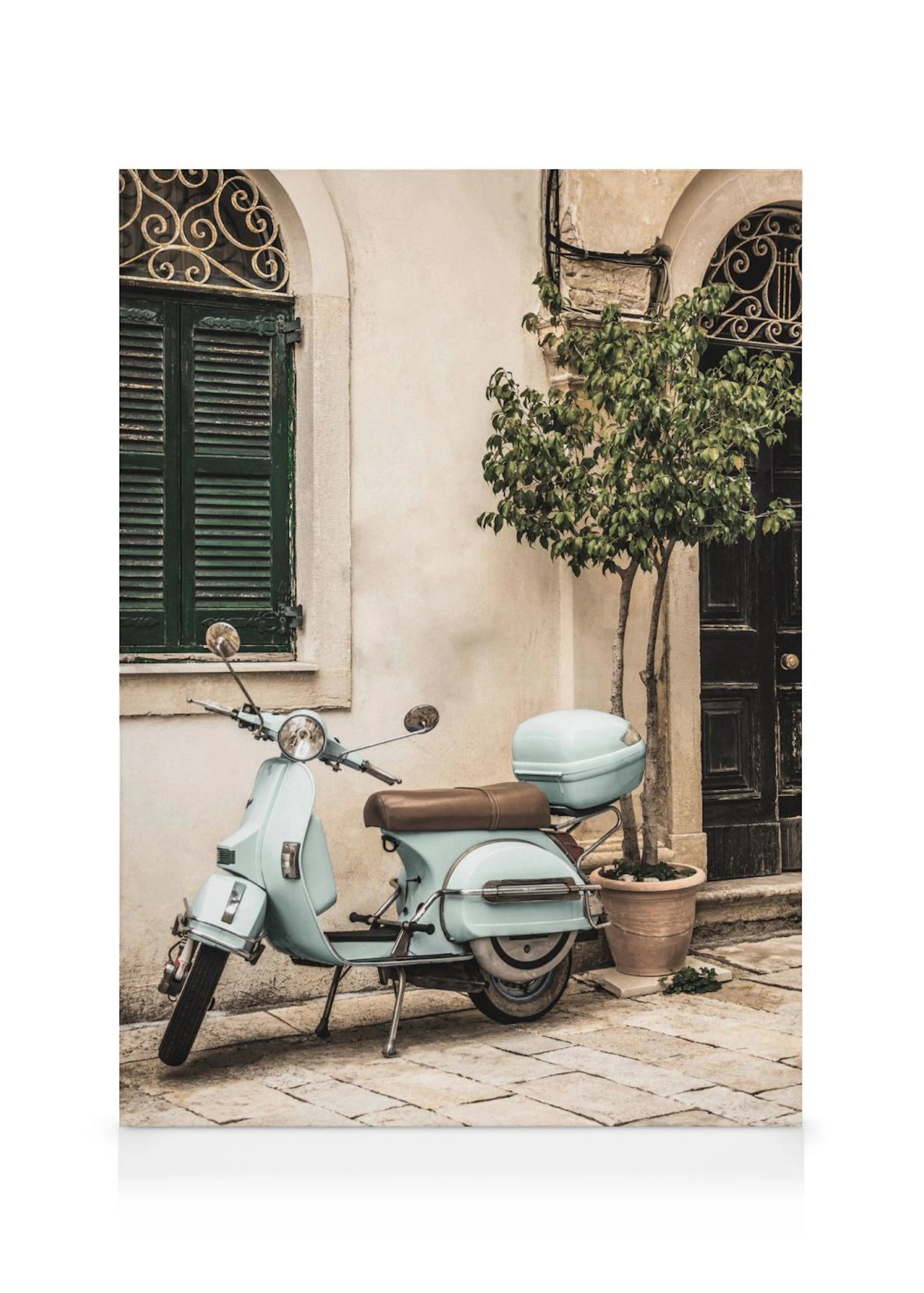 Obraz na plátně s tyrkysovou skútr Vespa s hnědým sedlem před historickou budovou se zelenými okenicemi a stromem v květináči.