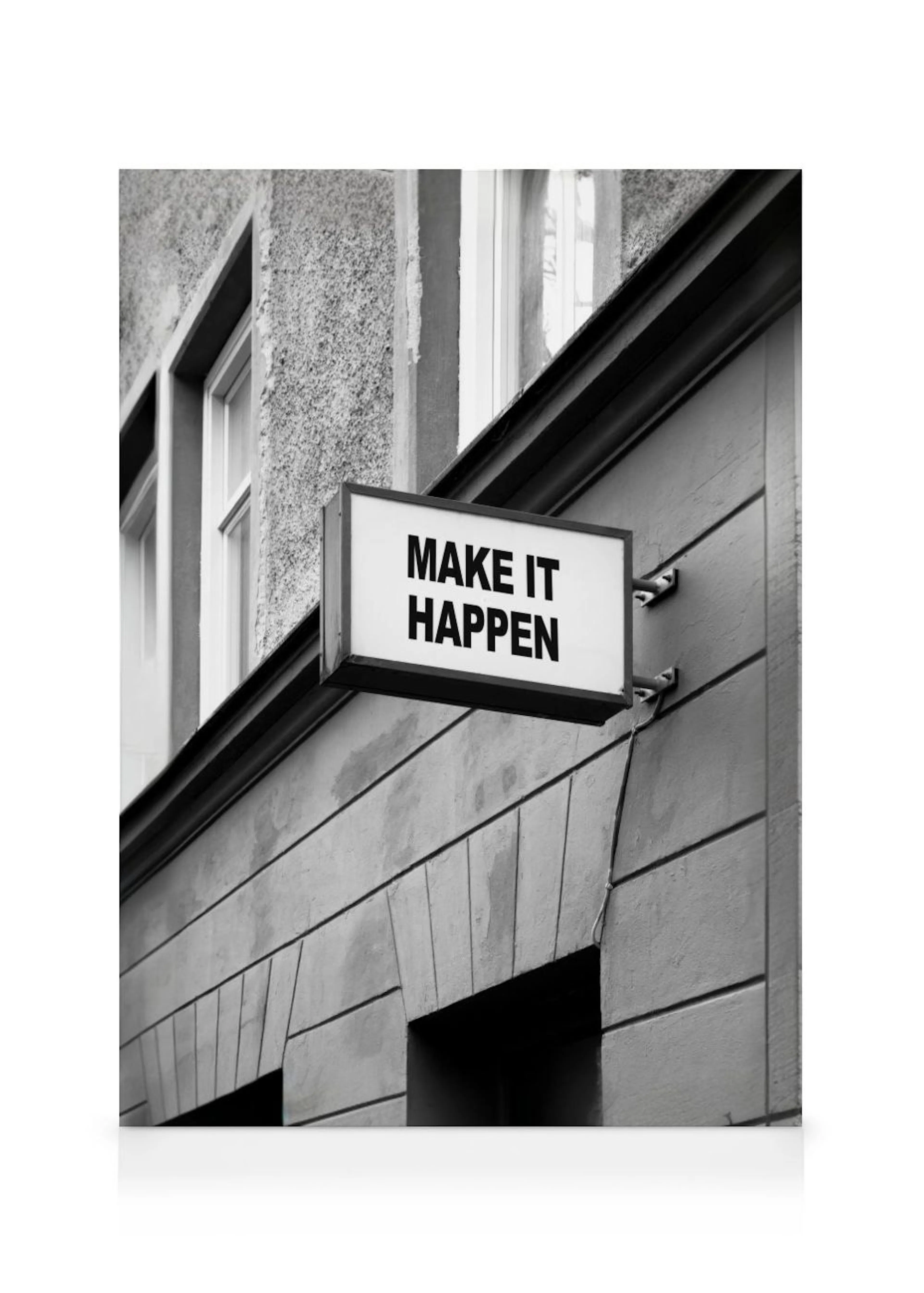 Lienzo monocromático de un letrero de MAKE IT HAPPEN en blanco y negro, sobre una pared gris.