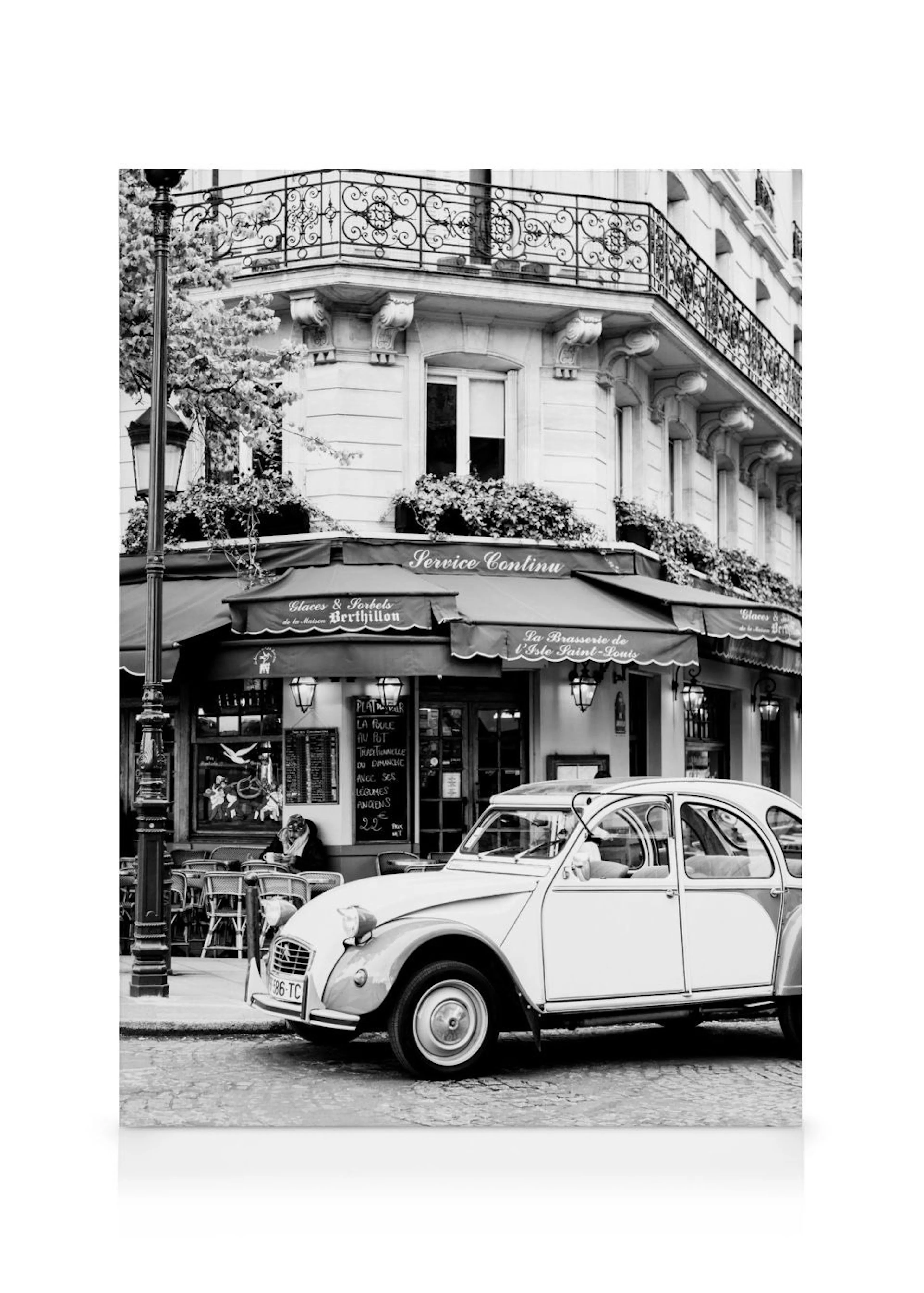Toile noir et blanc dune voiture vintage garée devant un café parisien classique avec des balcons en fer forgé.