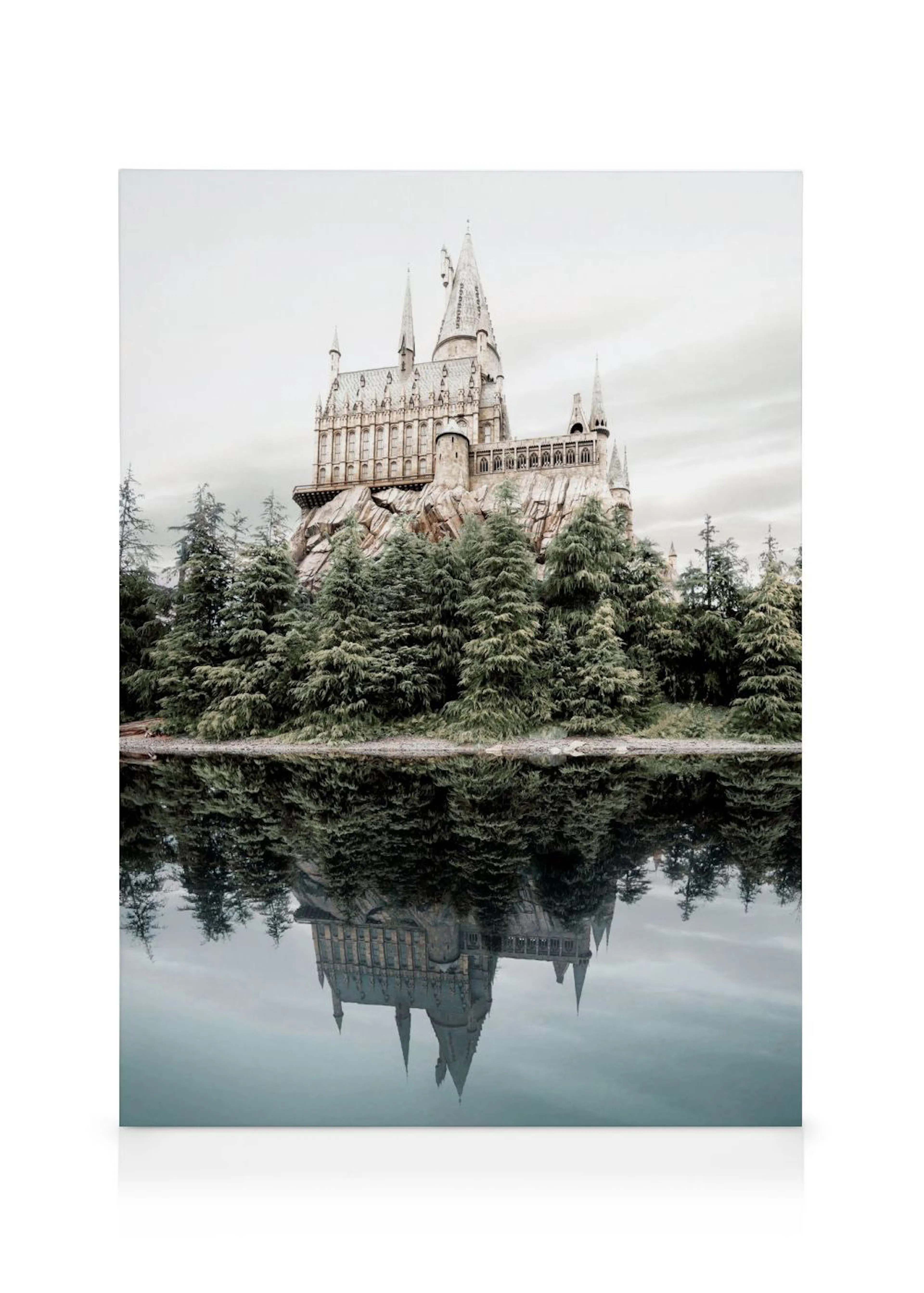 Lienzo del castillo de Hogwarts con pinos verdes y su reflejo en el agua, bajo un cielo gris.