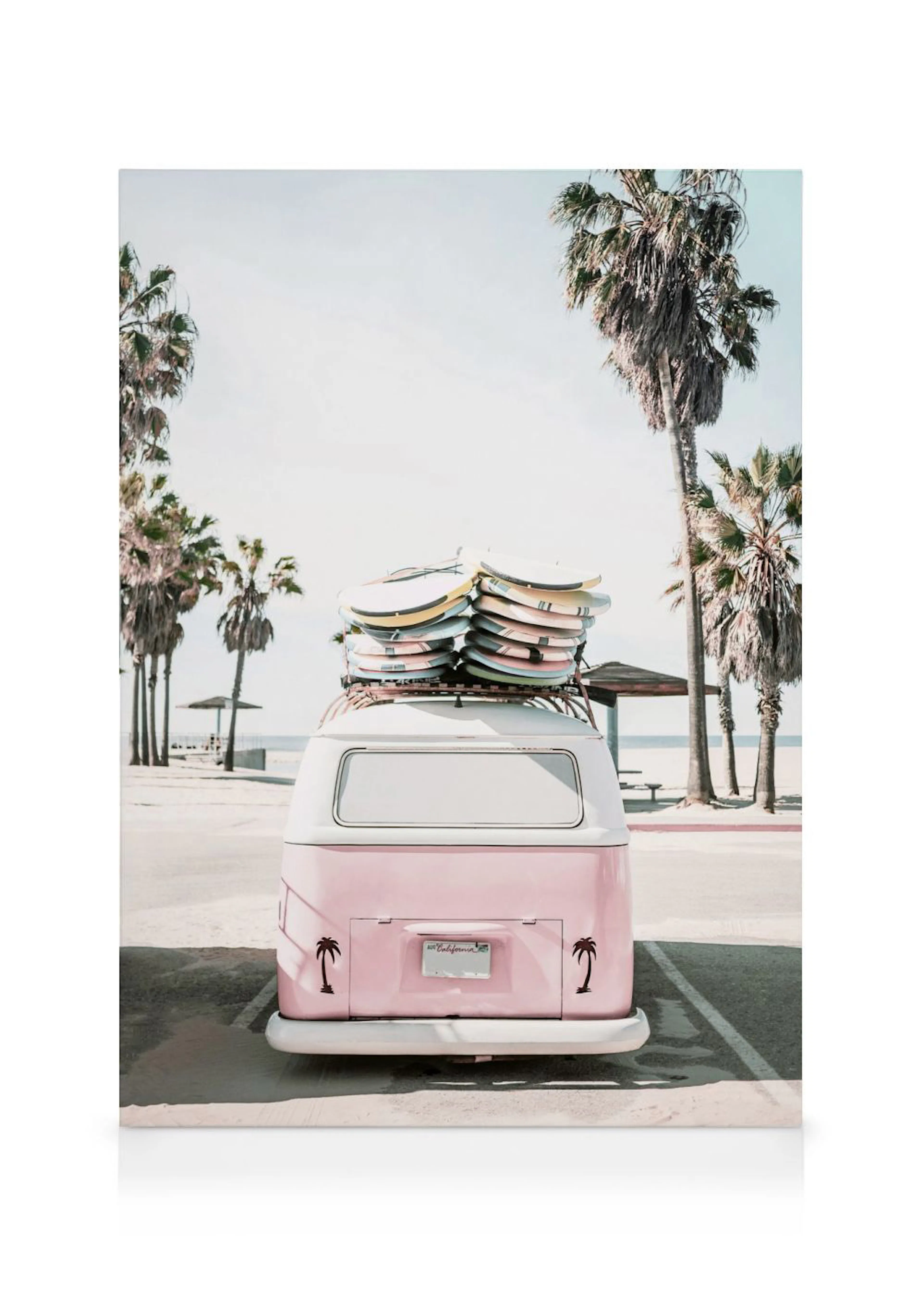 A canvas print featuring a light pink vintage van with surfboards on its roof, parked on a sandy road with palm trees and a beac