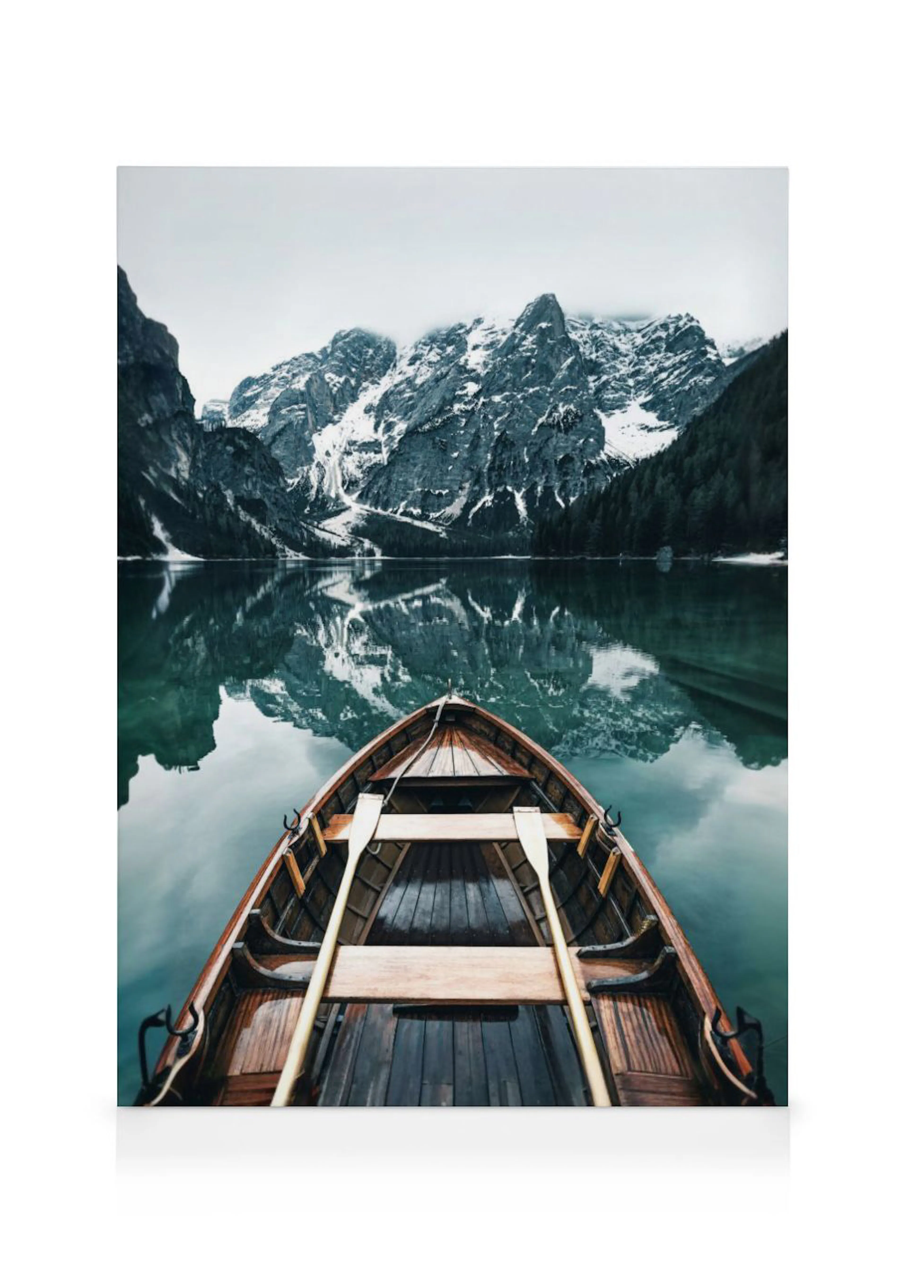 Stampa su tela di una barca in legno su un lago alpino con montagne innevate e alberi che si riflettono sullacqua.