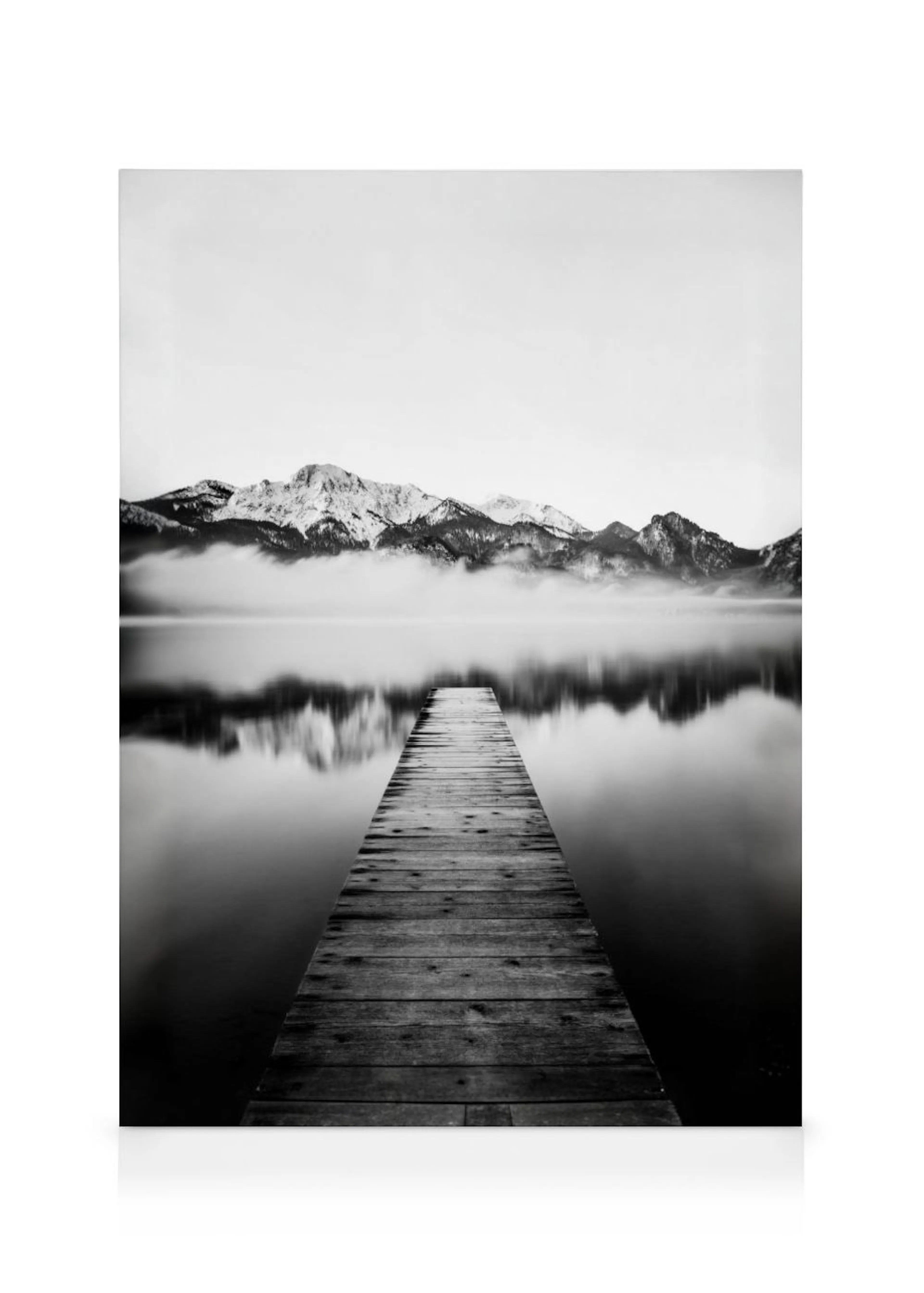 Monochrome canvas of a wooden pier extending into a calm lake with snow-capped mountains and misty reflections.