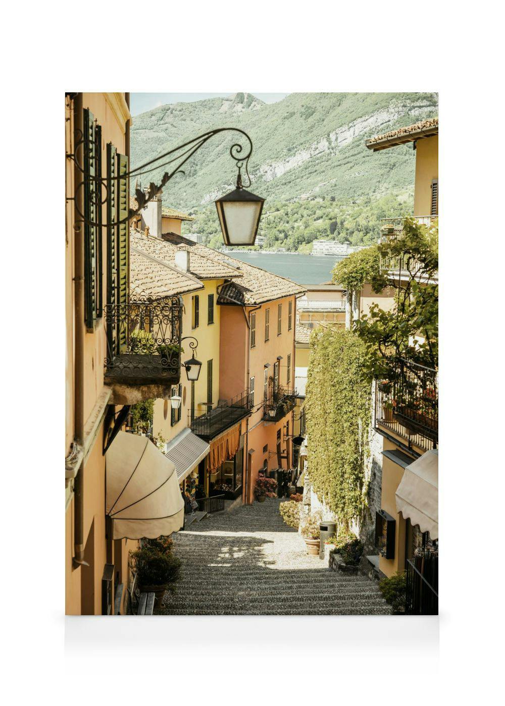 A canvas showing a narrow stone staircase leading down through a colorful European village to a lake and mountains in the backgr