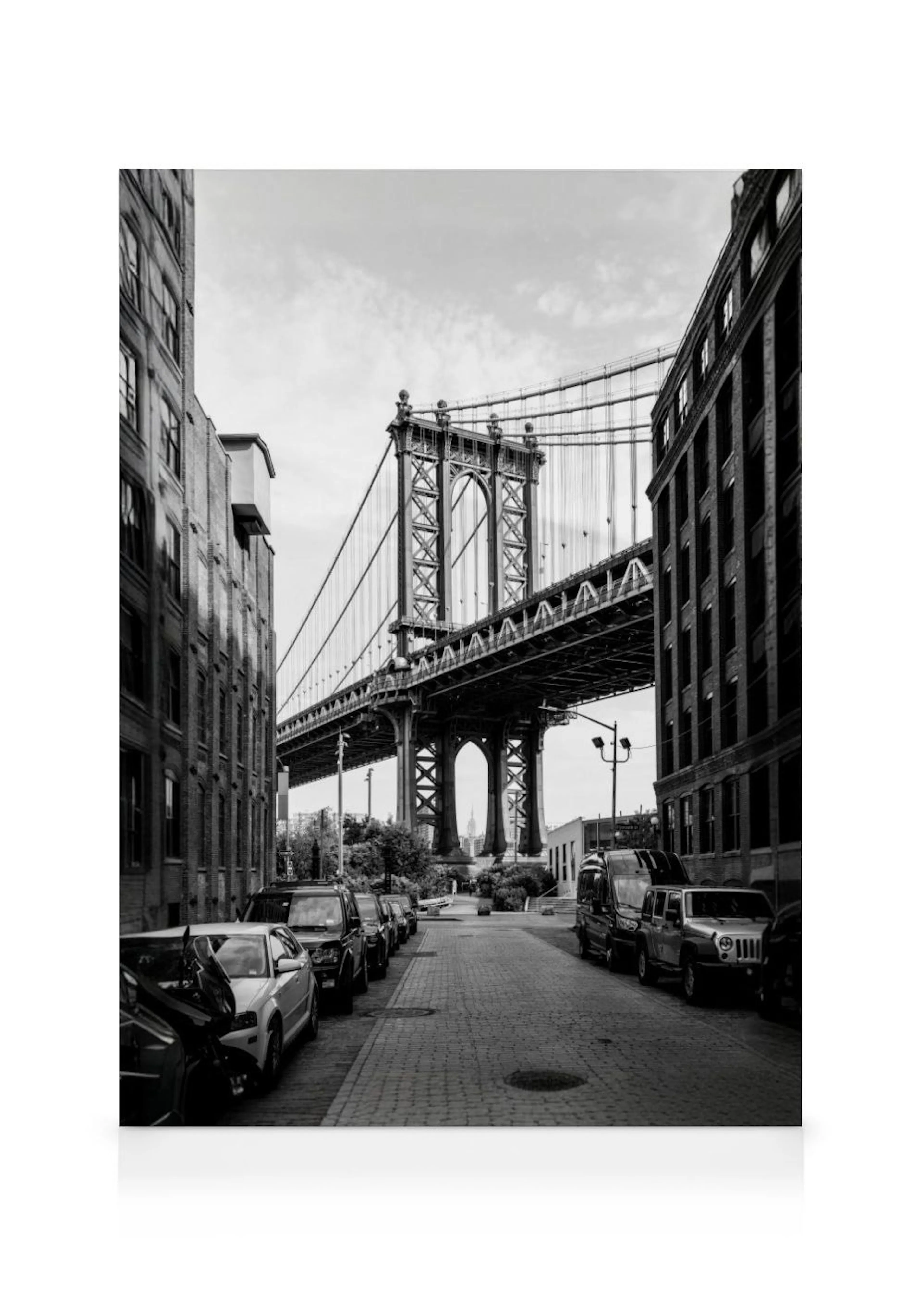Et lærred af Manhatten Bridge i sort/hvid set fra gaden med parkerede biler og bygninger langs fortovet.