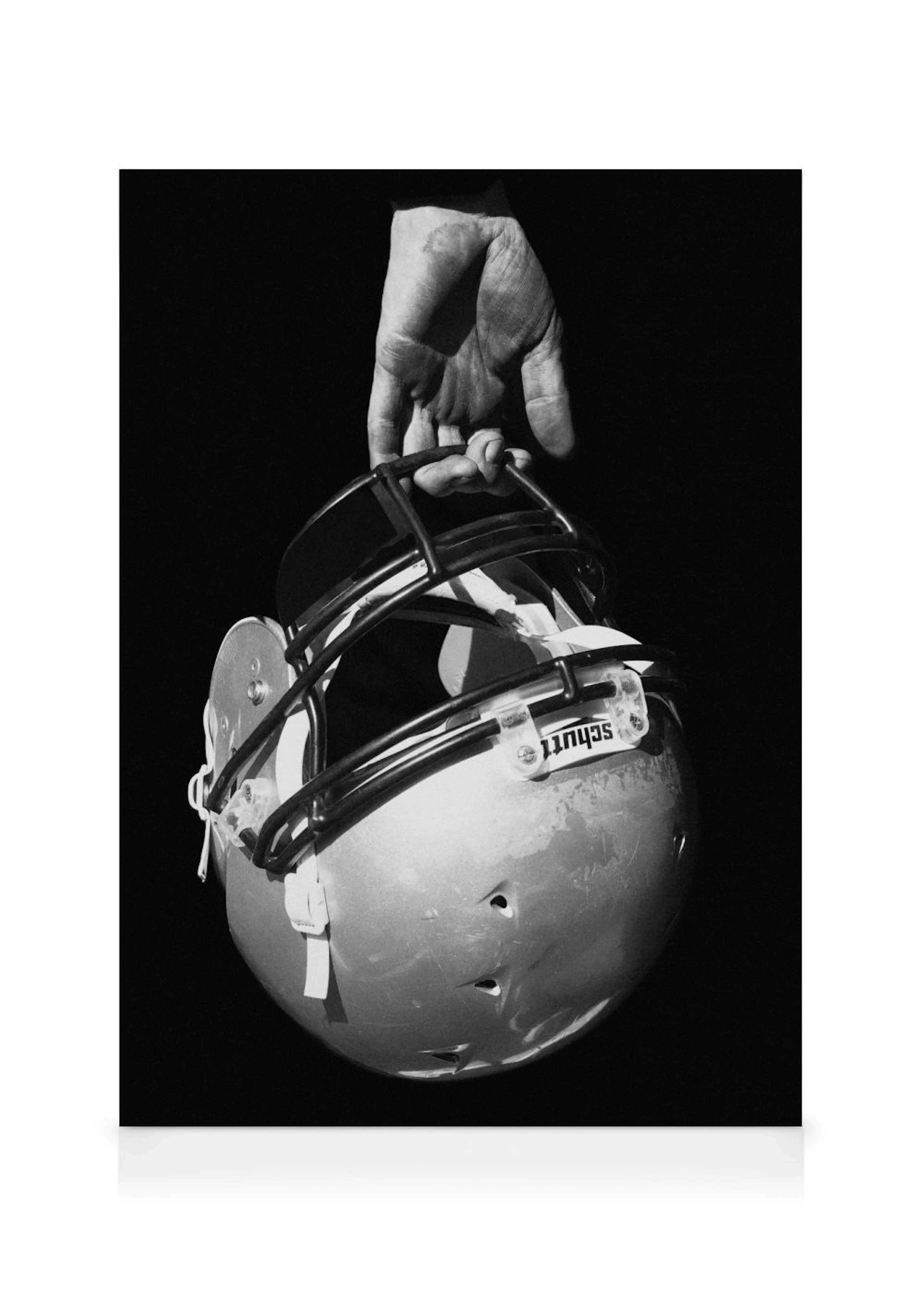 Toile en noir et blanc dune main tenant un casque de football américain Schutt contre un fond sombre.