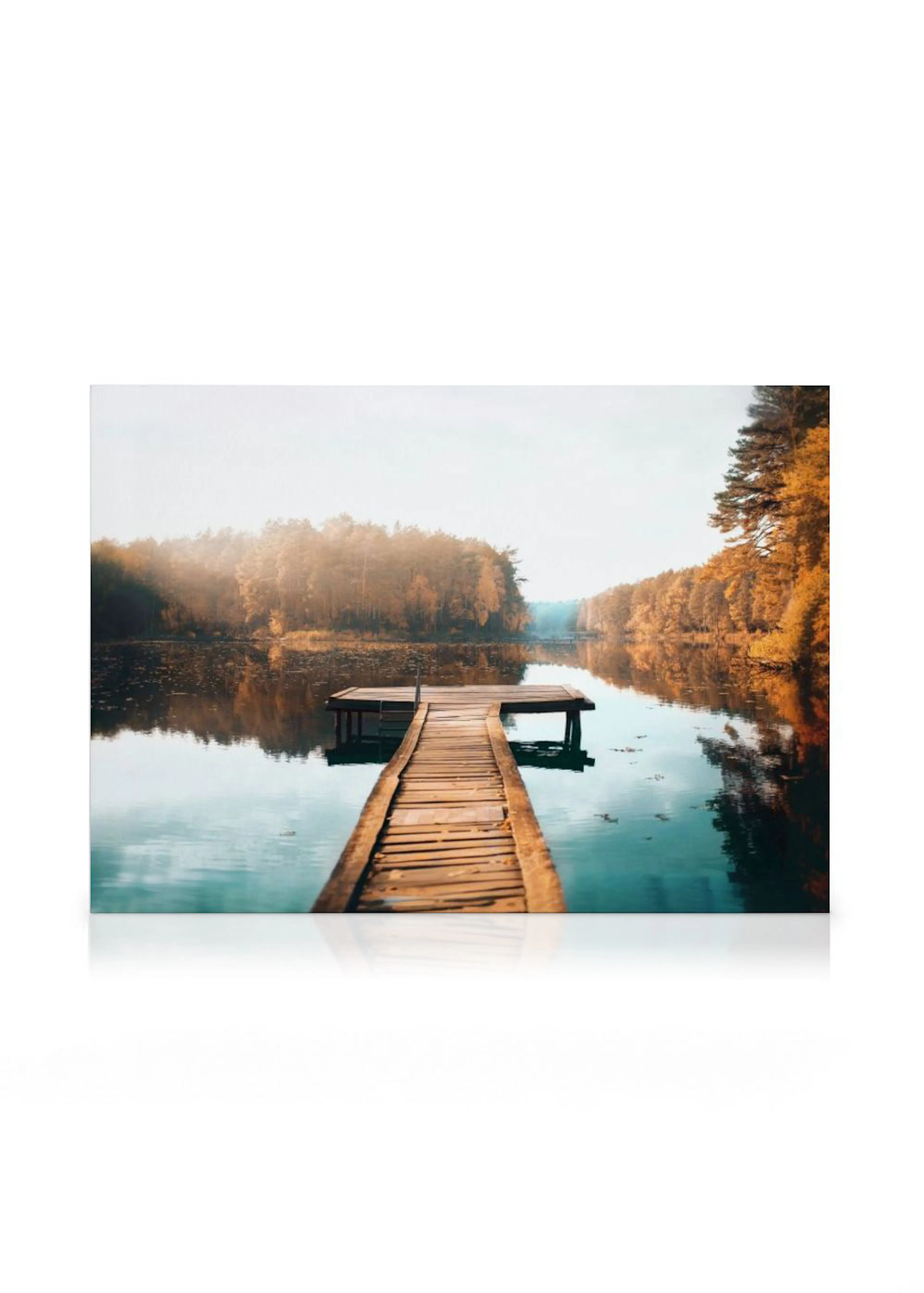 Leinwandbild mit einem Holzsteg, der in einen ruhigen See mit herbstlichen Bäumen am Ufer ragt, in sanftem Licht.