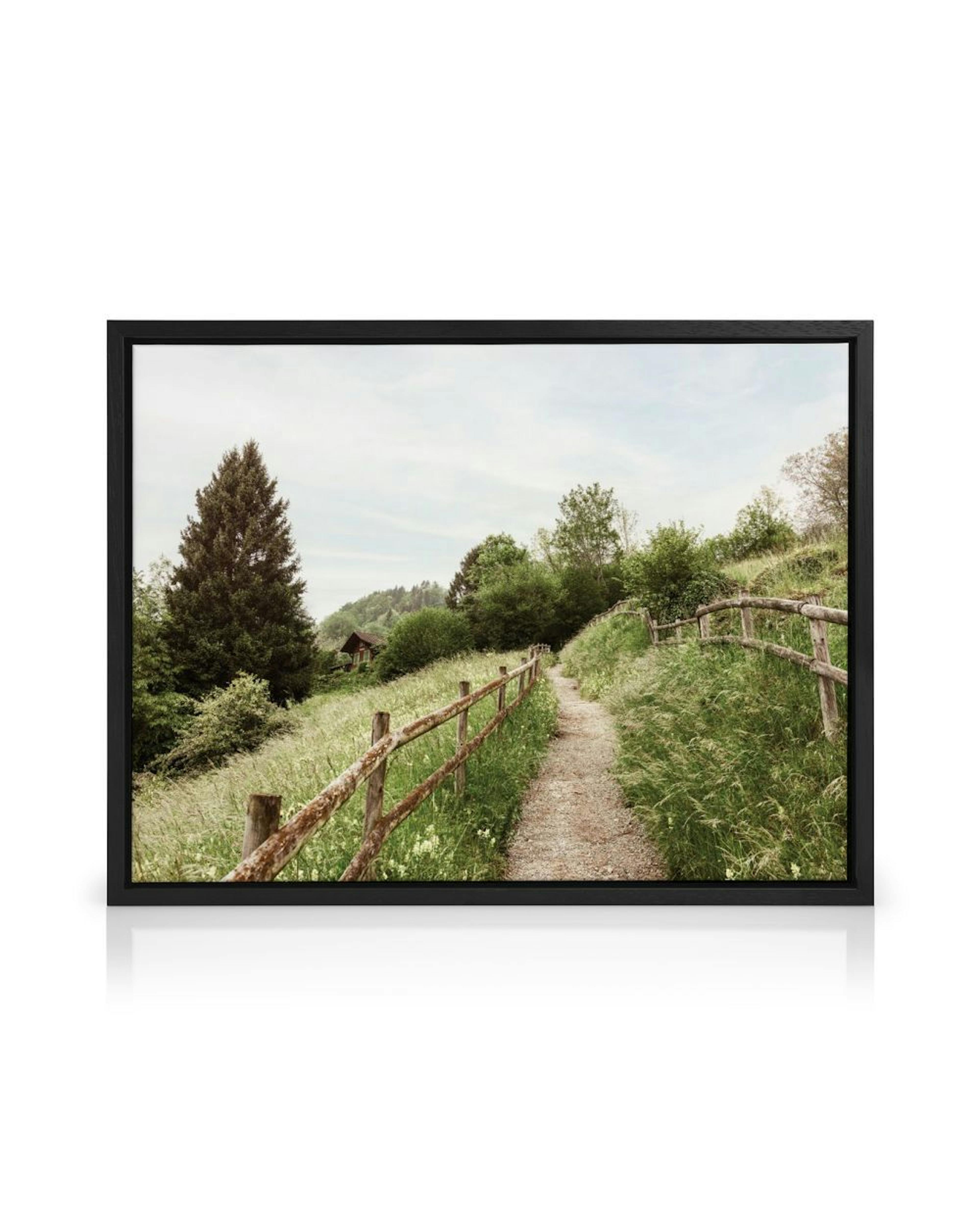 A canvas of a winding path with a rustic fence through a green field, hanging in a bright, minimalist room.