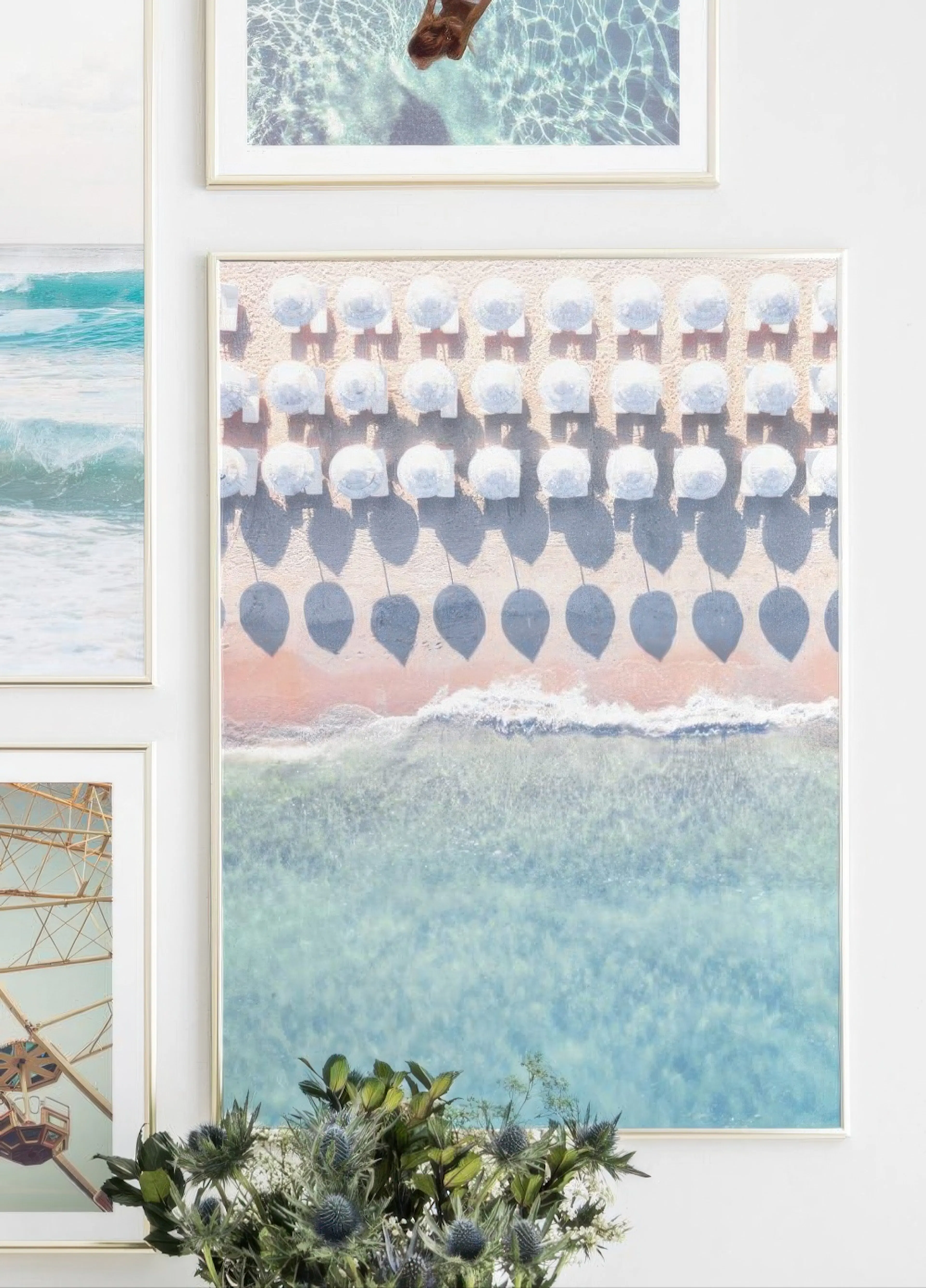 An aerial beach poster with white umbrellas on pink sand and clear blue ocean, displayed on a gallery wall.