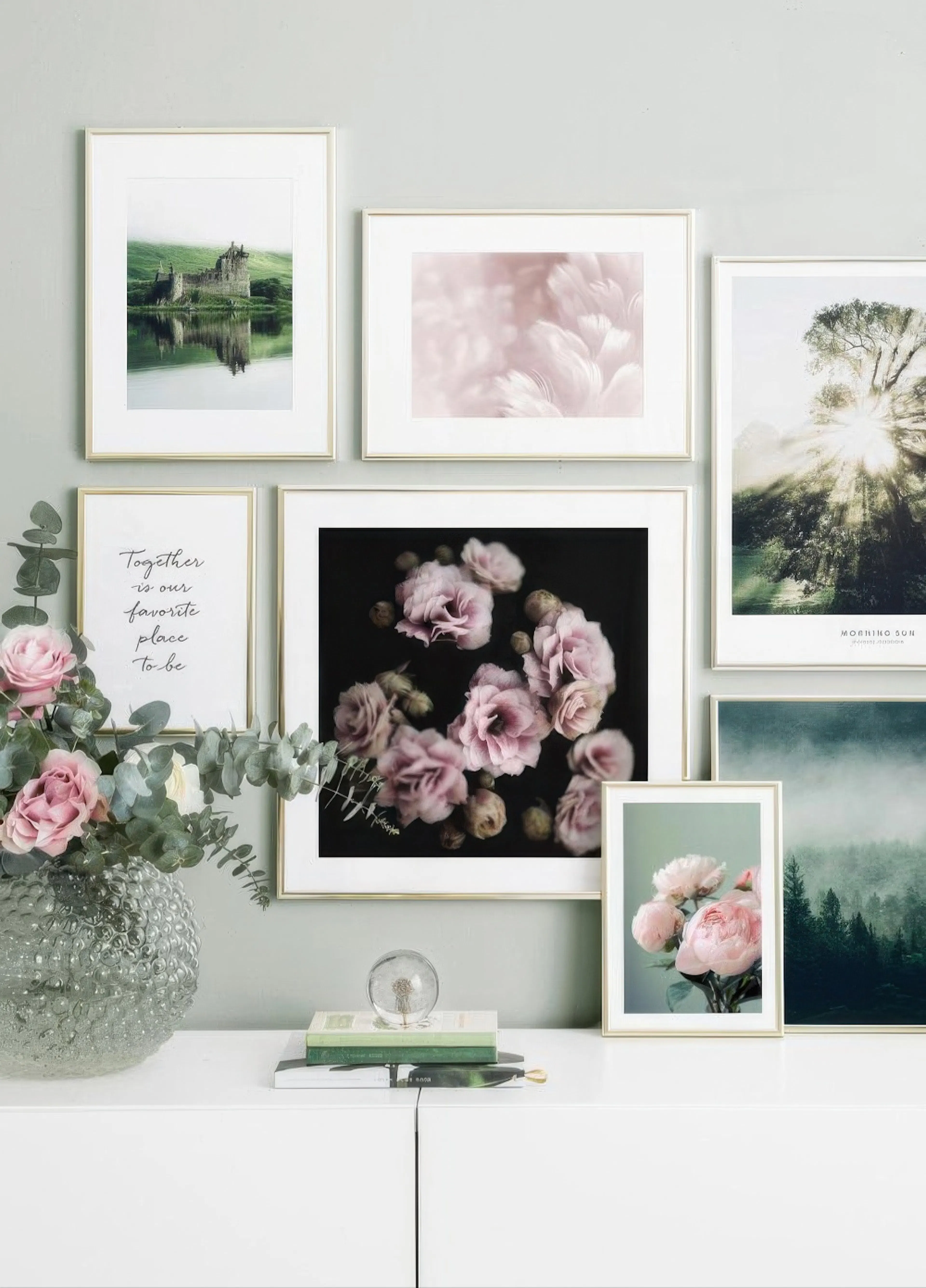 A gallery wall with various posters, including a castle, pink feathers, pink flowers, and a misty forest, displayed above a whit