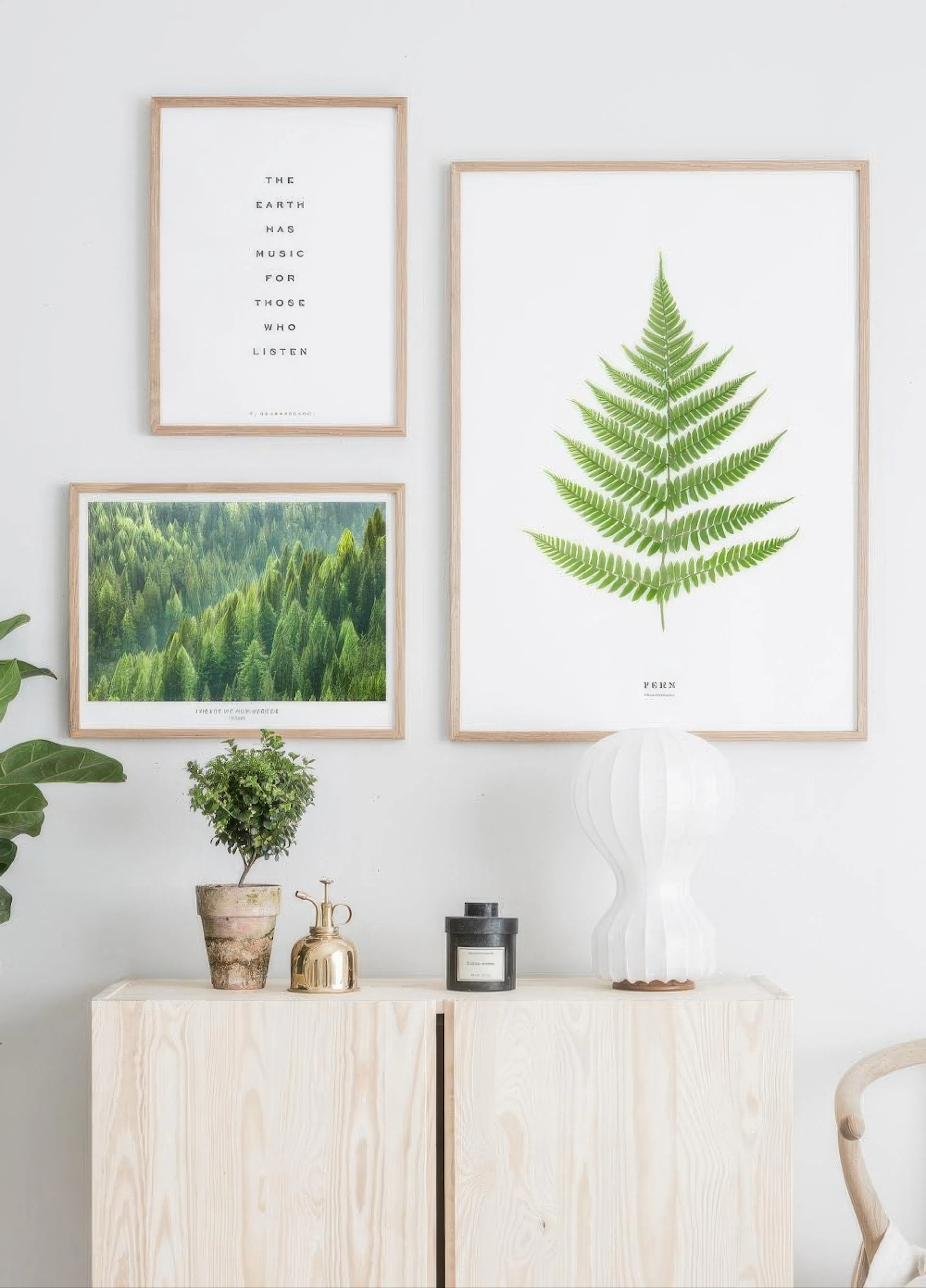 A gallery wall with three posters: a text poster, a green fern poster, and a forest poster, displayed above a wooden cabinet.