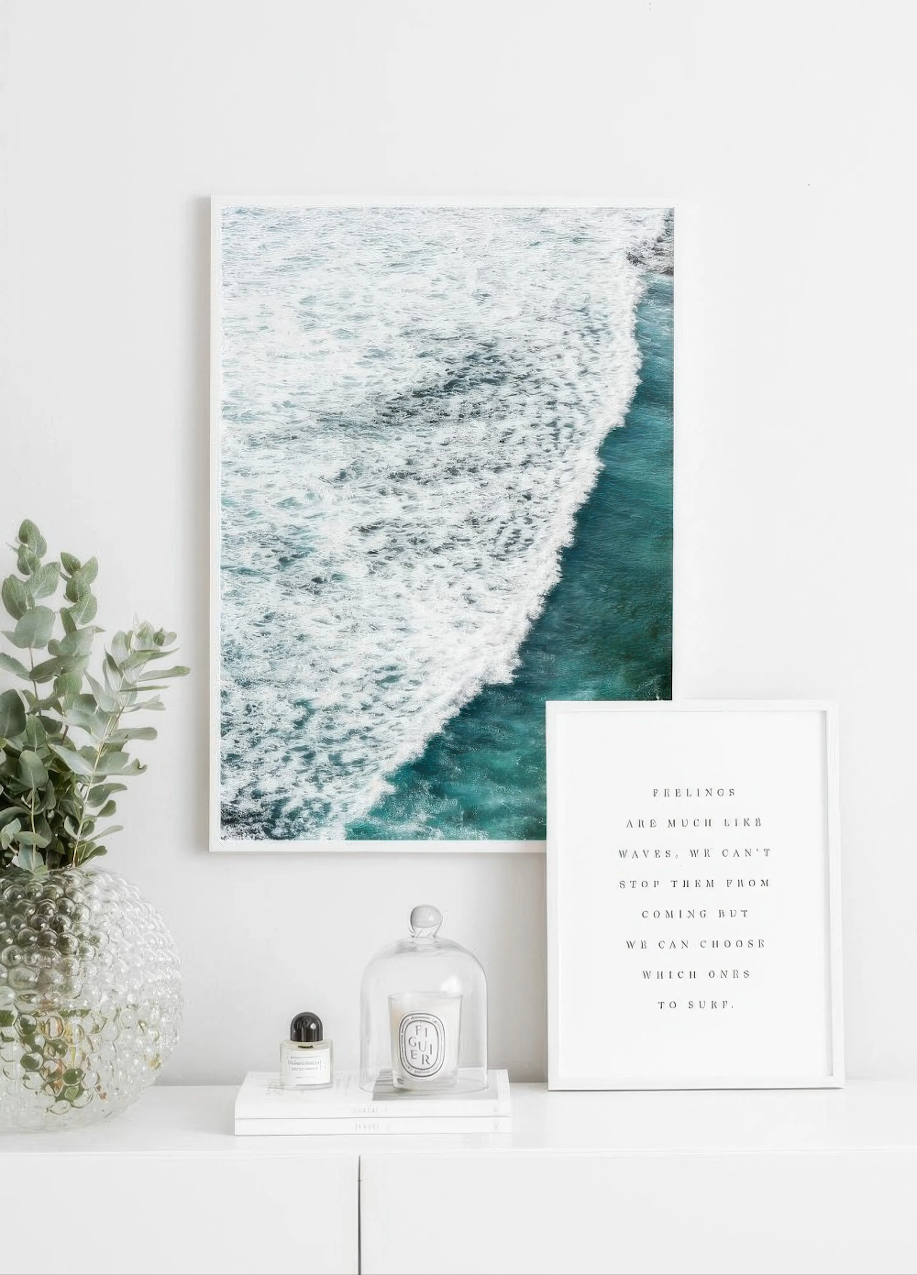 A poster featuring a foamy ocean wave breaking on a turquoise sea, displayed above a white dresser with a plant and home decor.