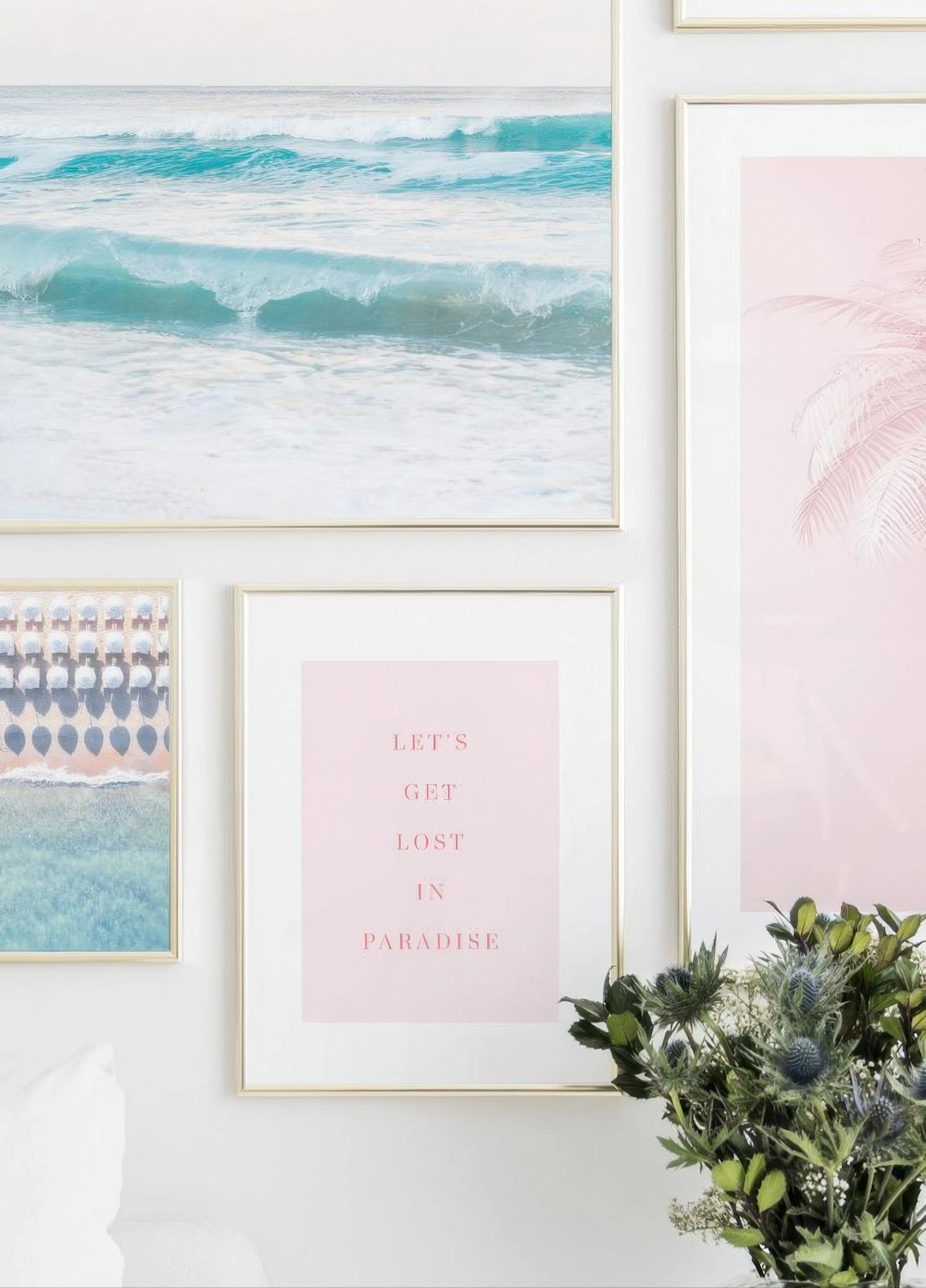A gallery wall with a blue ocean wave poster, a pink palm tree poster, and a pink poster with the text Lets Get Lost in Paradise